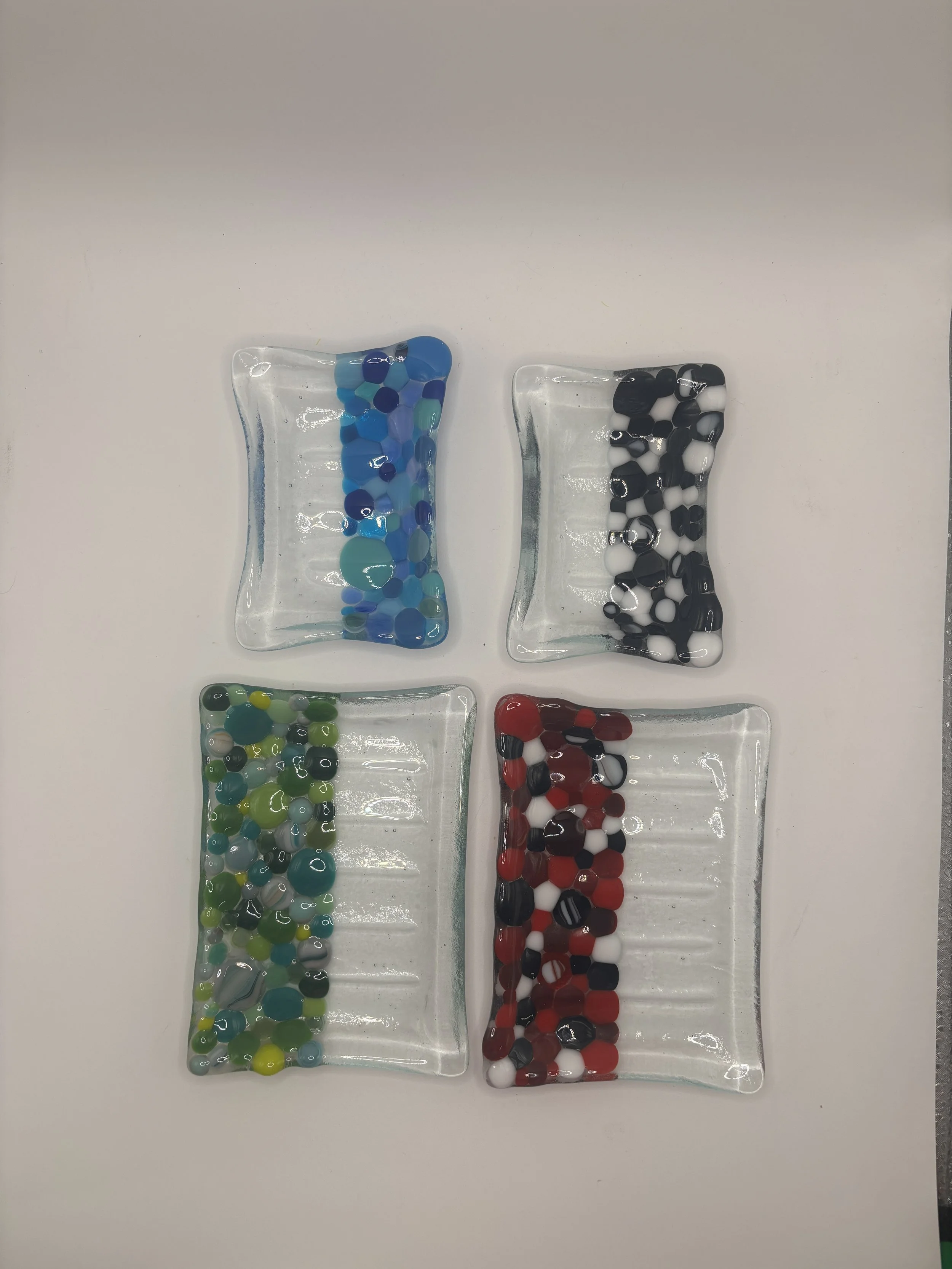 Four small glass dishes with multicolored glass beads arranged in a row on a white surface.