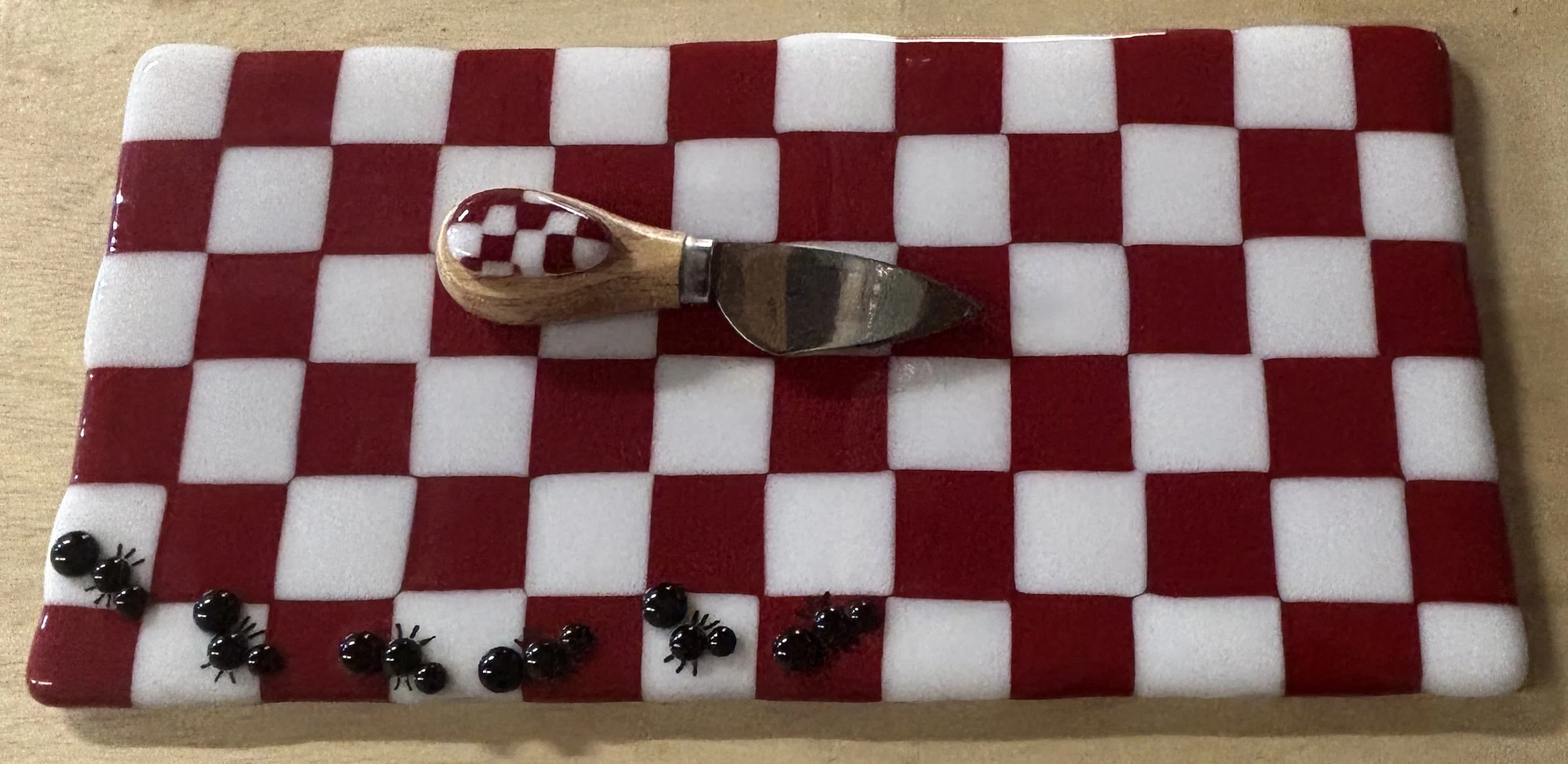 A chocolate checkerboard cake decorated with black edible bugs and a small plastic knife with a parasitic checkerboard pattern.