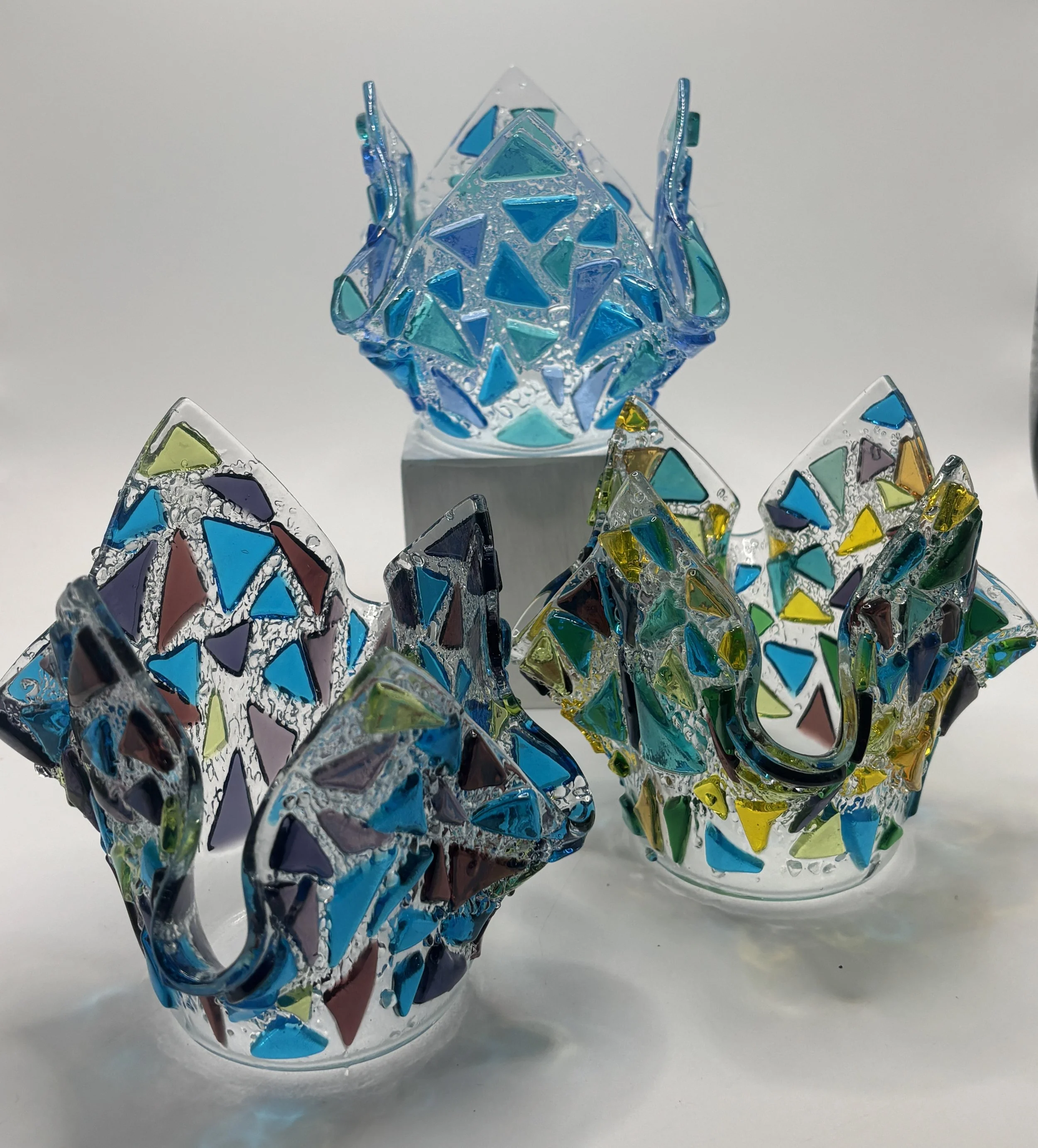 Colorful glass sculptures resembling butterflies and abstract shapes, arranged in a display against a plain background.