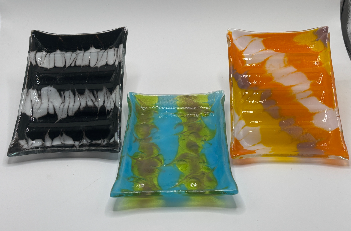 Three colorful glass plates with abstract designs, placed on a white surface.