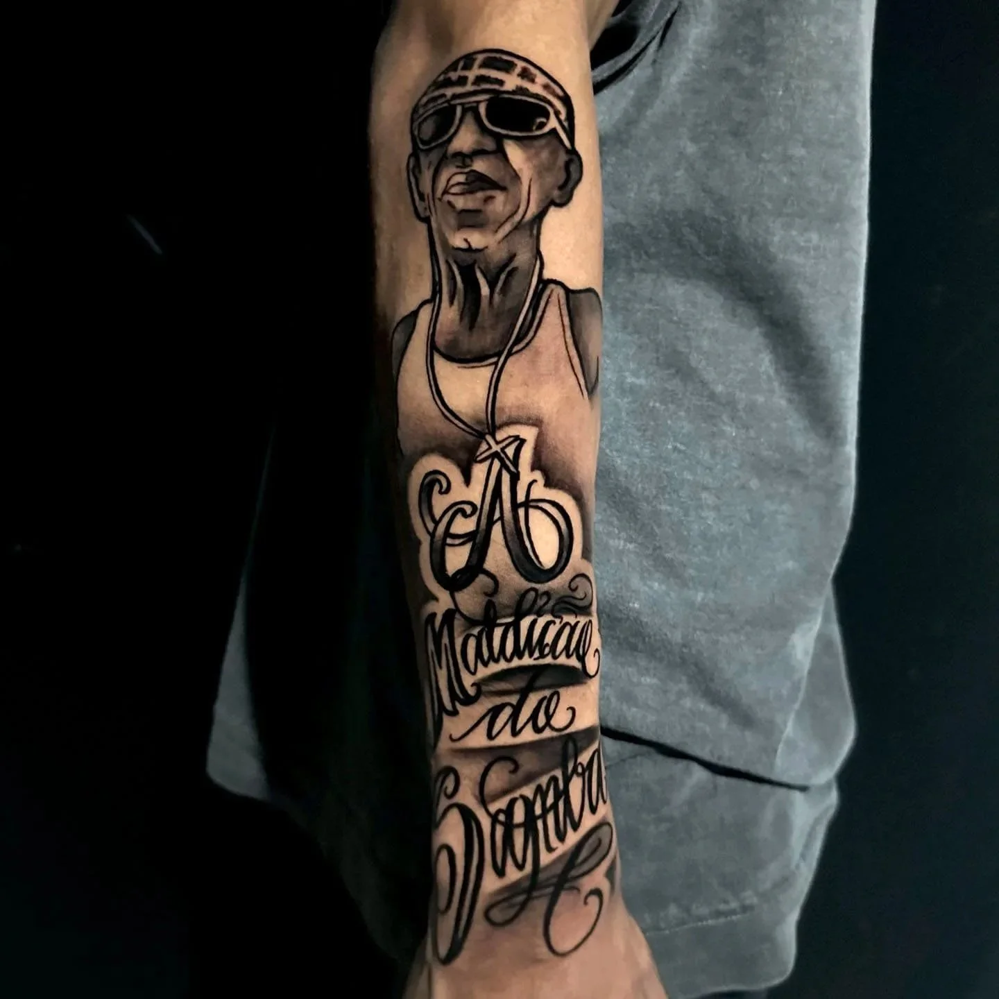 A tattoo on a person's forearm depicting a man wearing sunglasses, with text that reads 'Małpa' and additional script.