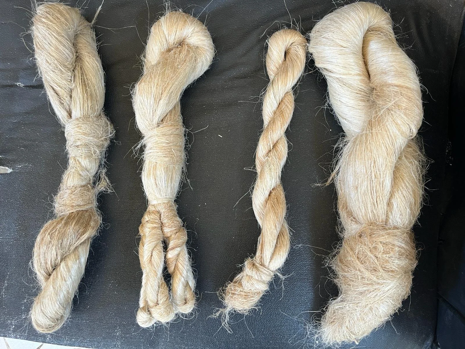 Four bunches of blonde hair, each twisted or braided, laid out on a black surface.