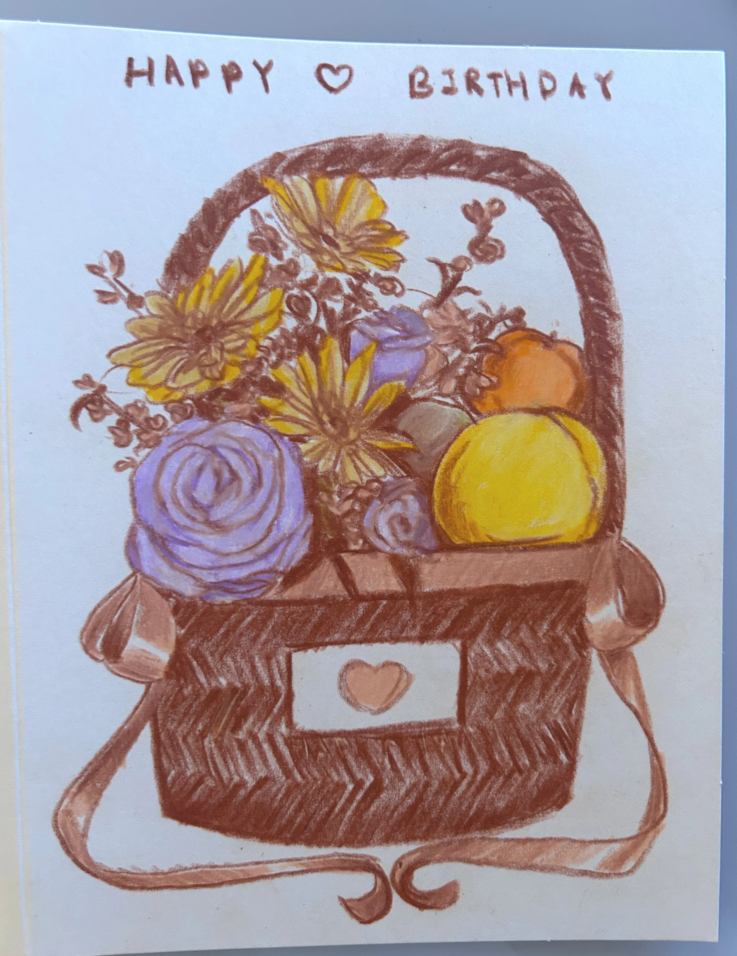 A hand-drawn birthday card with a basket of flowers and a heart-shaped button. The top of the card says 'HAPPY LOVE BIRTHDAY' in brown writing.
