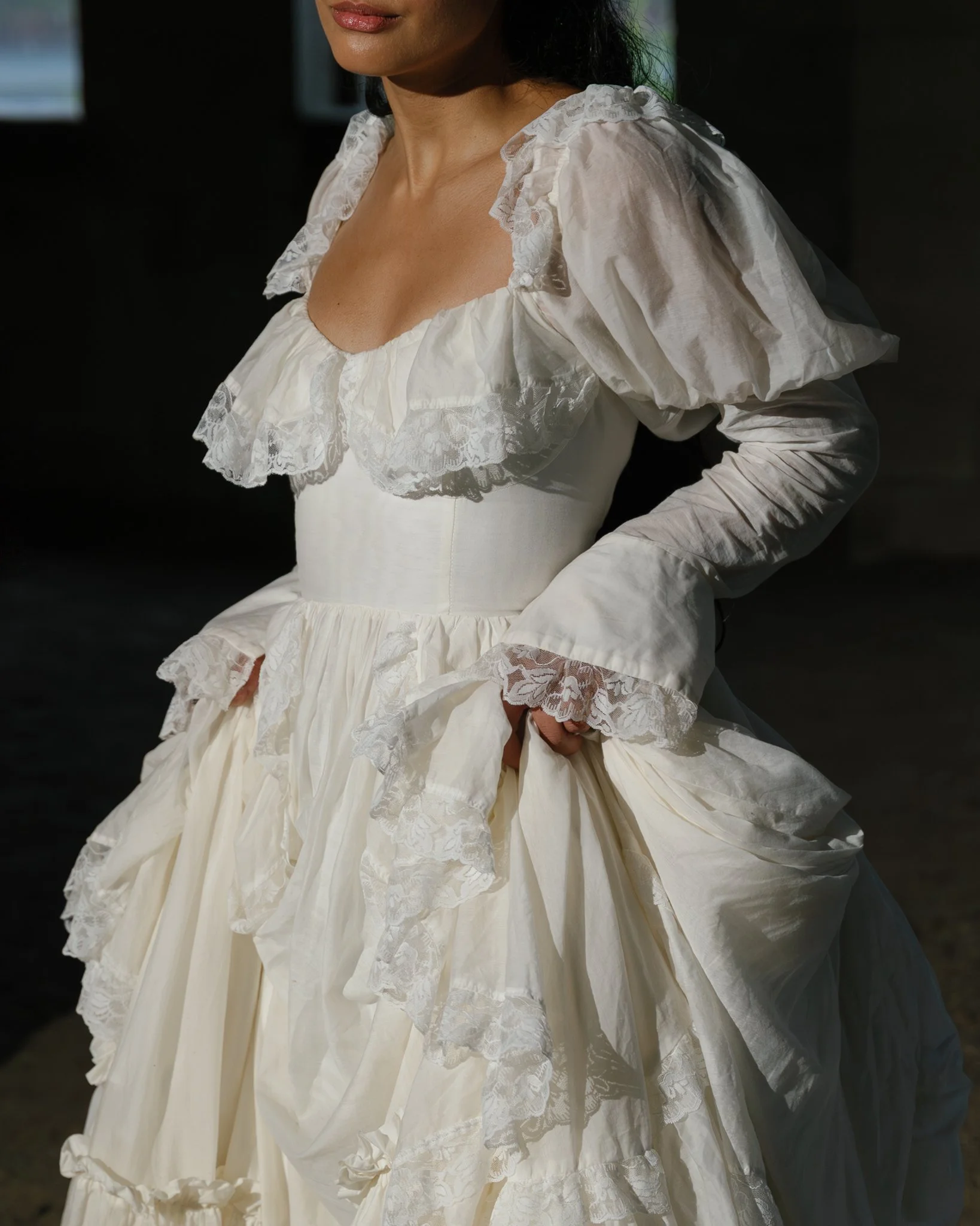 A woman wearing a vintage-style white dress with lace details and ruffled sleeves.