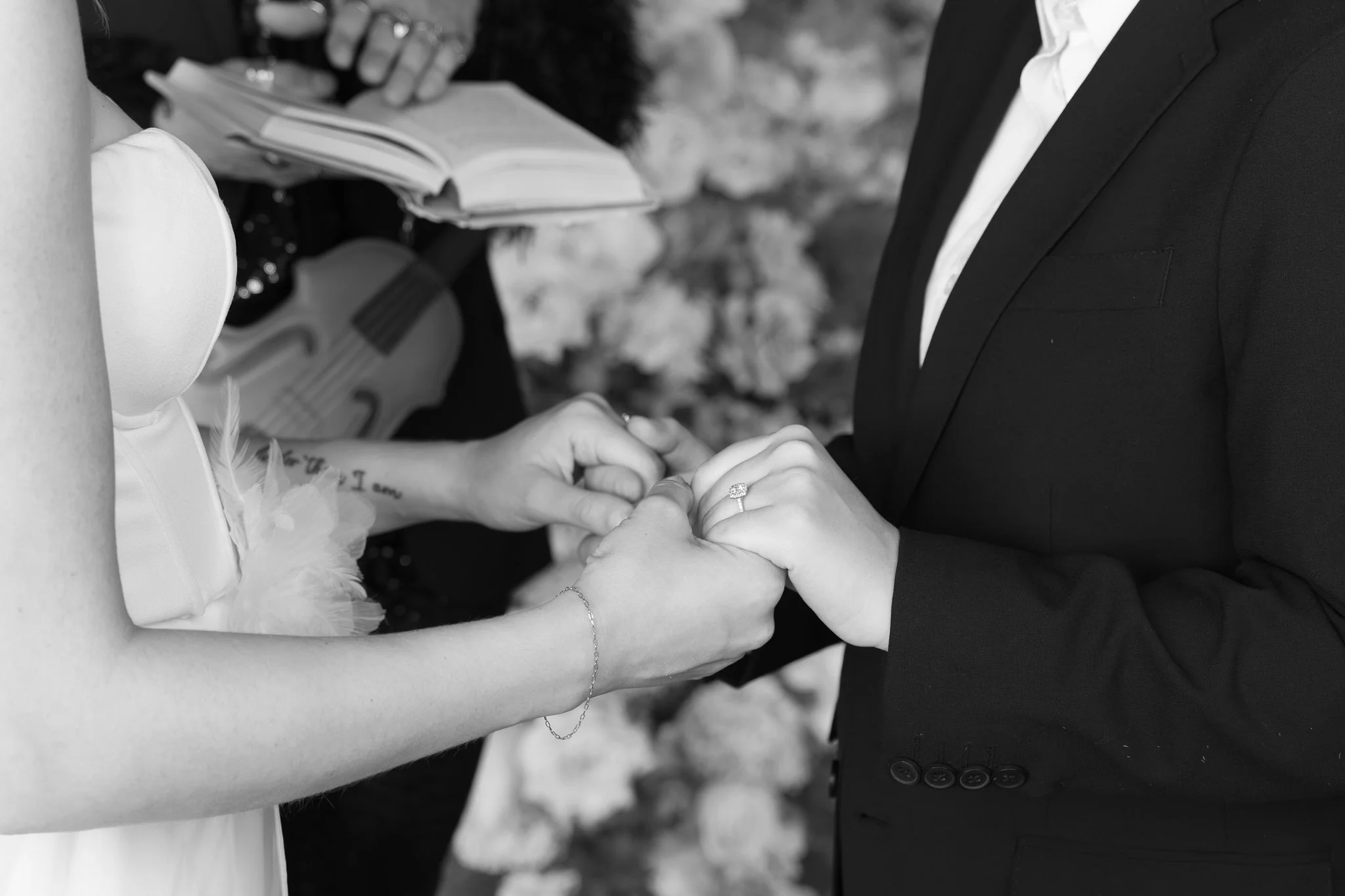 A bride and groom holding hands during their wedding ceremony, with the bride wearing a dress and the groom in a suit.