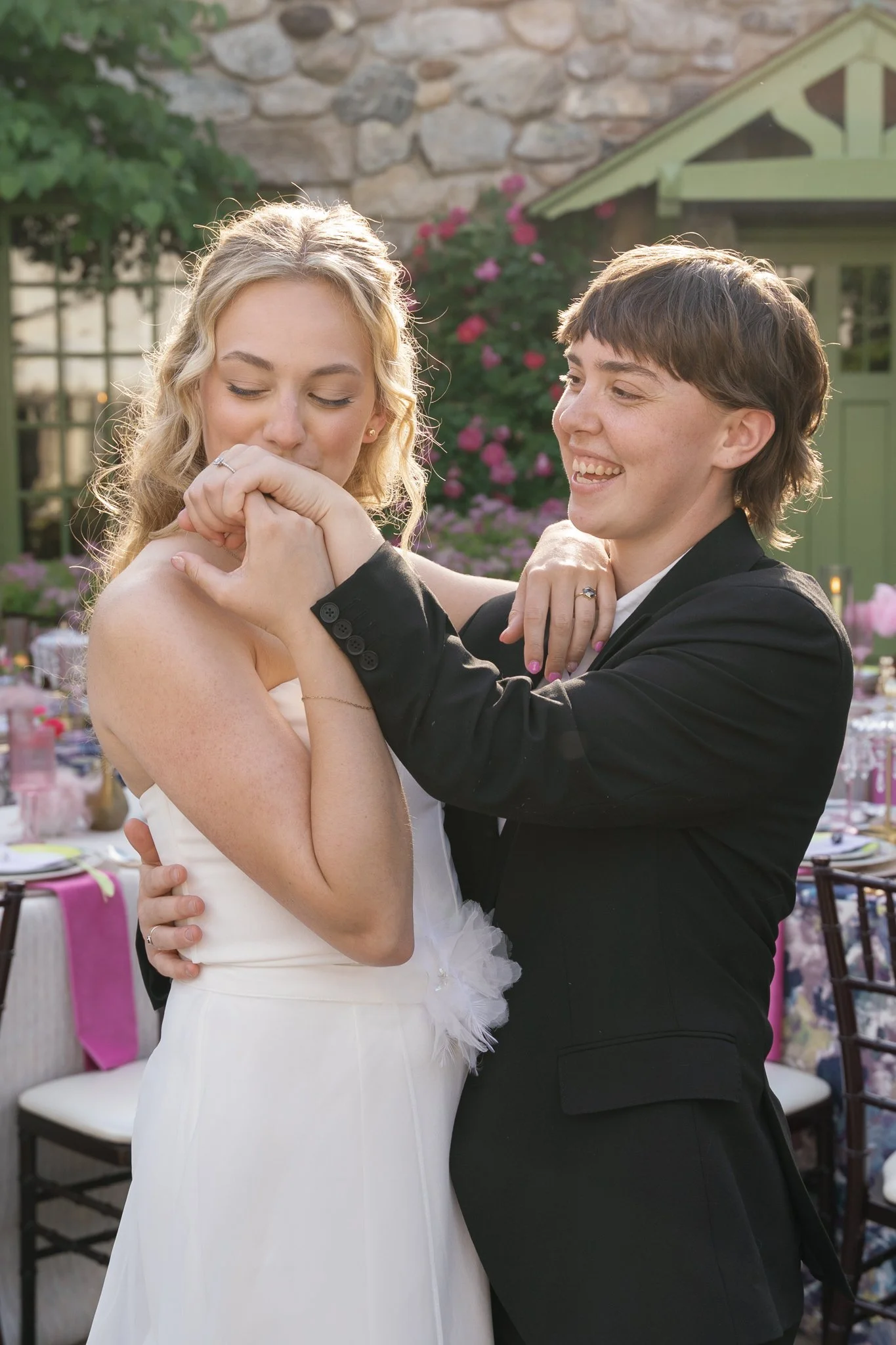 A couple dancing closely at an outdoor event with decorated tables and pink flowers in the background.