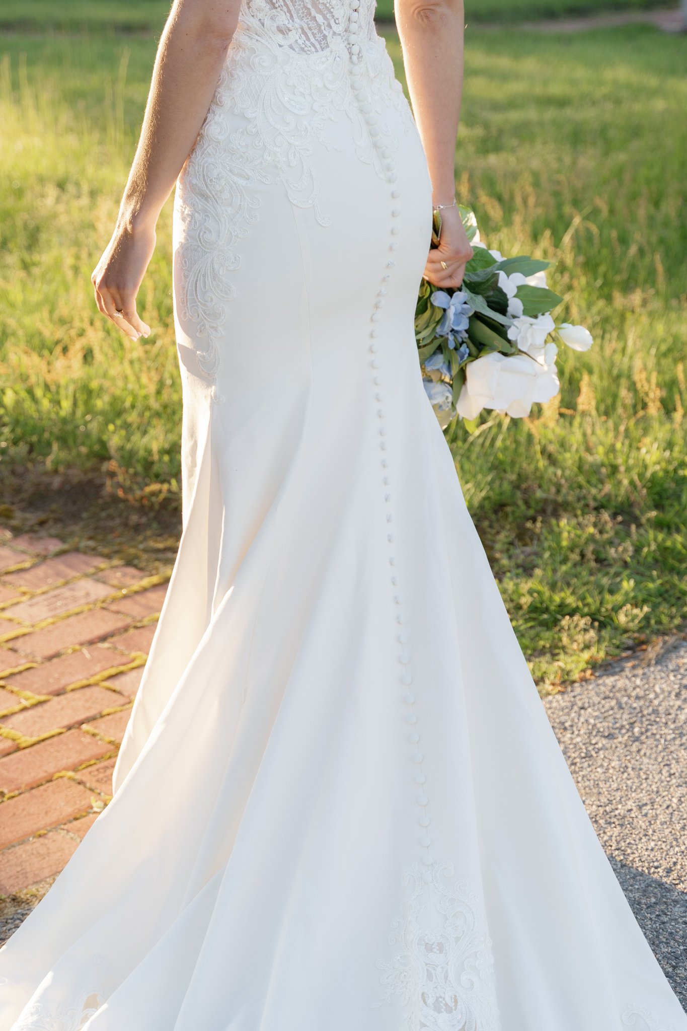 Close-up of a bride wearing a white wedding dress holding a bouquet of white flowers in a grassy outdoor setting.