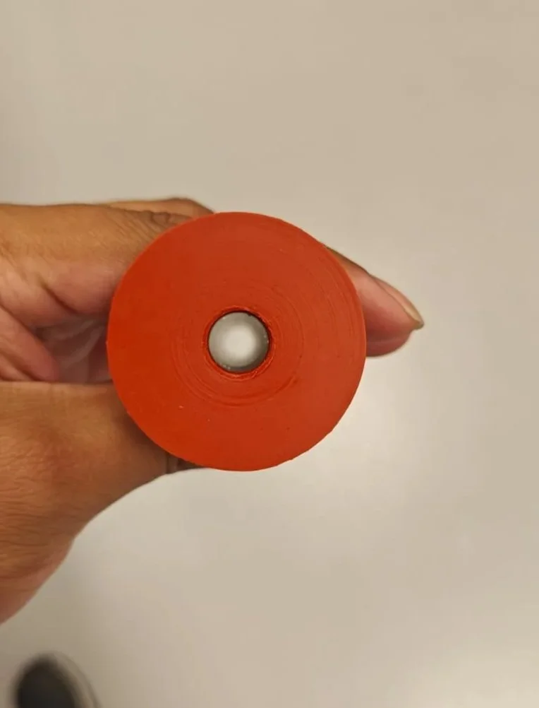 Mano sosteniendo un rollo de cinta adhesiva de color naranja contra un fondo de pared clara.