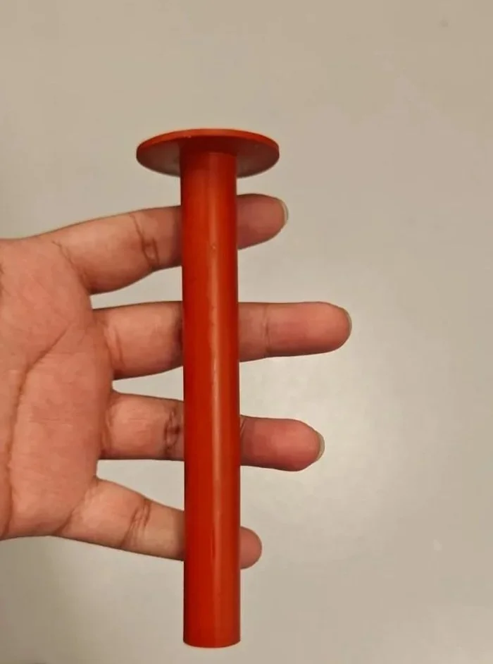 Una mano sosteniendo un cilindro naranja con una base plana en un fondo gris claro.