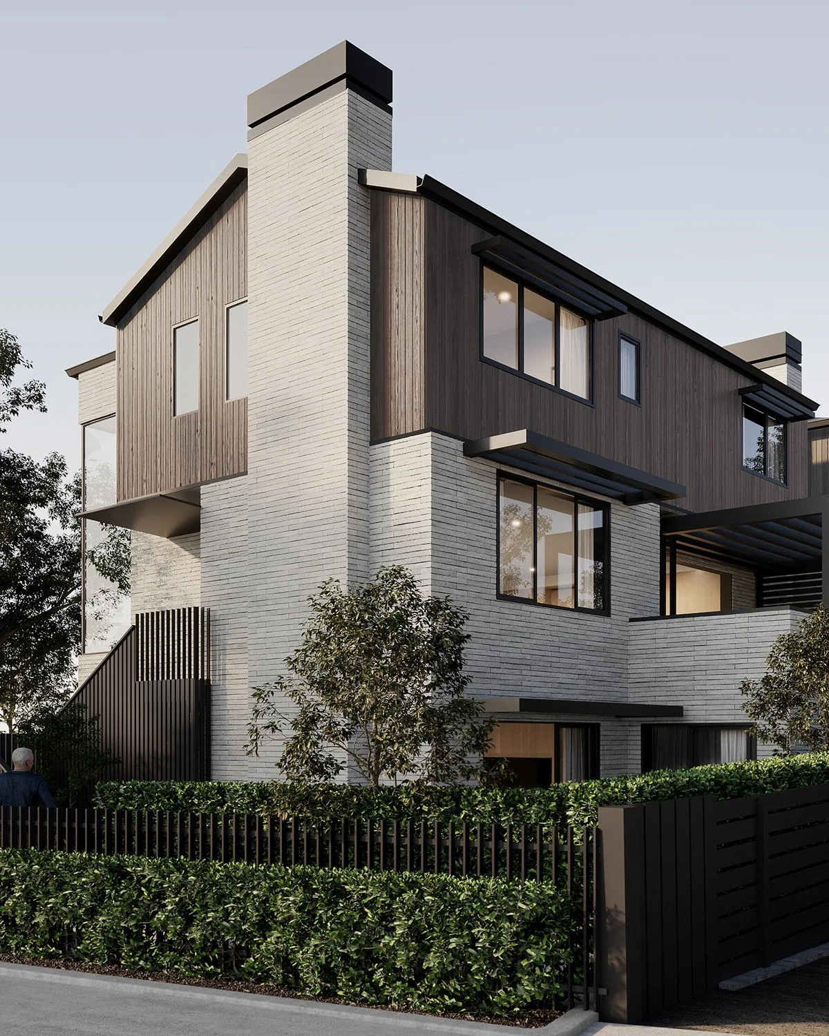 Modern multi-story house with white brick and dark wood siding, large windows, and a black fence with greenery in front.
