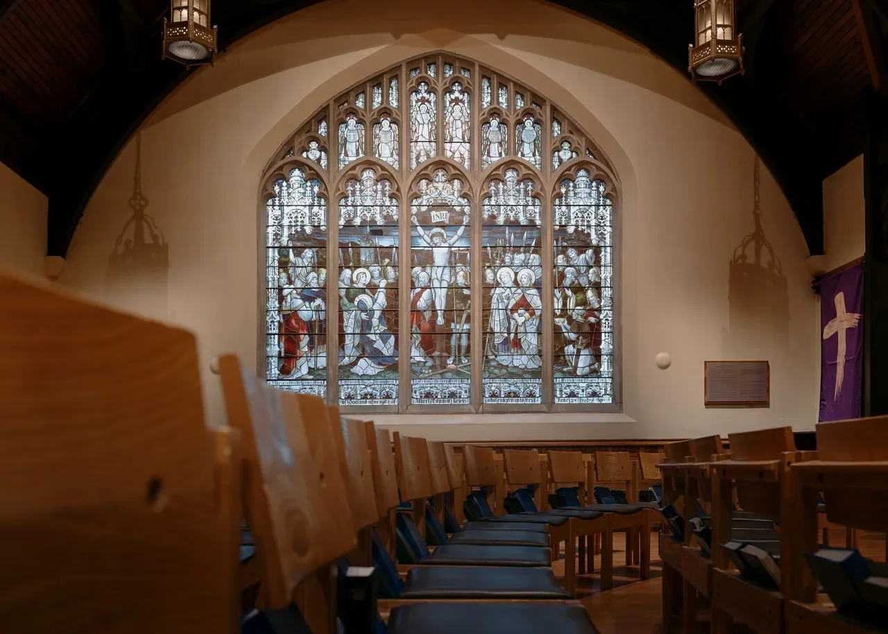 Traditional church interior with a large stained glass    window and wooden pews, a classic chapel venue for a celebration of life or funeral service
