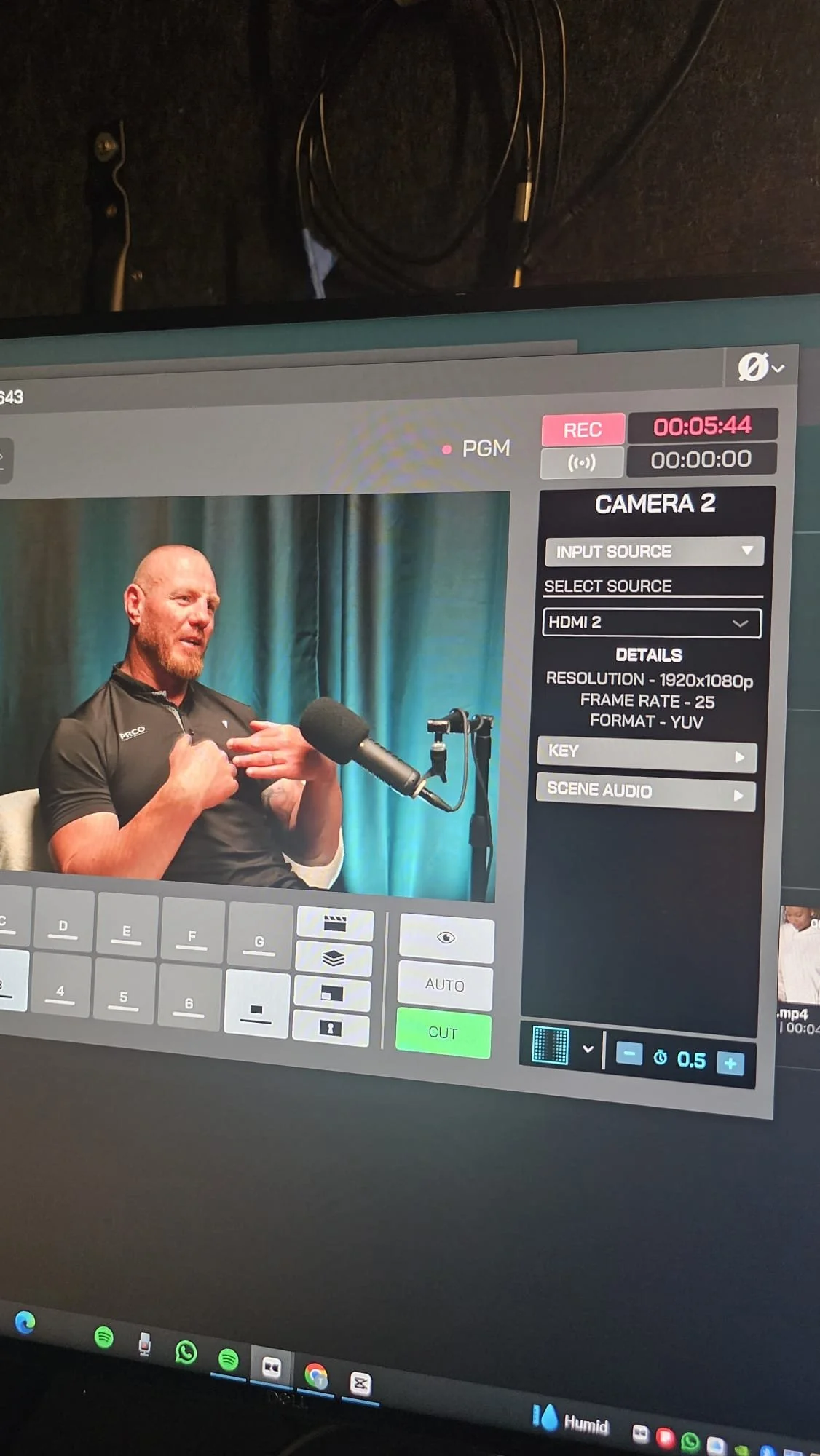 A camera monitor displaying a man with a beard and a bald head speaking into a microphone during an interview or recording session.