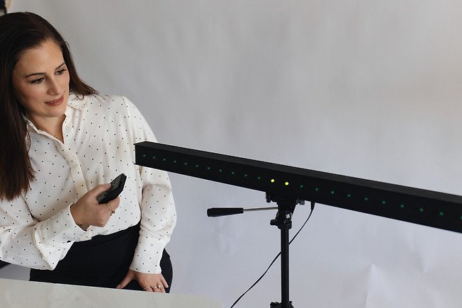 Woman in white polka dot shirt holding a remote and looking at a laser beam test device.
