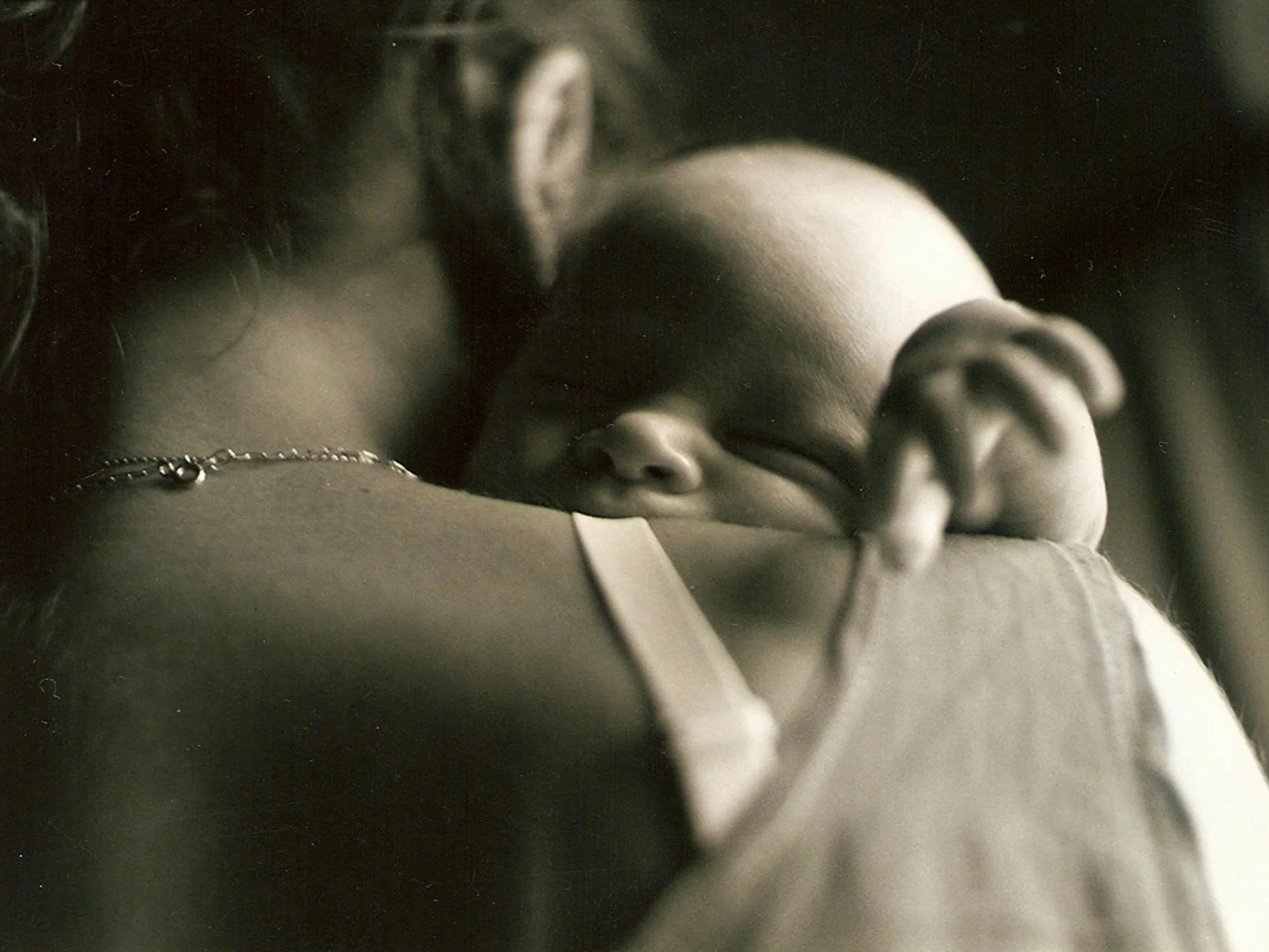 Close-up of a person's face and arm resting on a surface, wearing earrings, a bracelet, and a ring, in black and white.