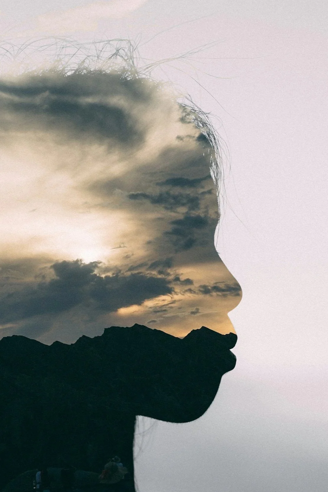 A double exposure photograph combining the silhouette of a woman's face in profile with a cloudy sky and mountain landscape.