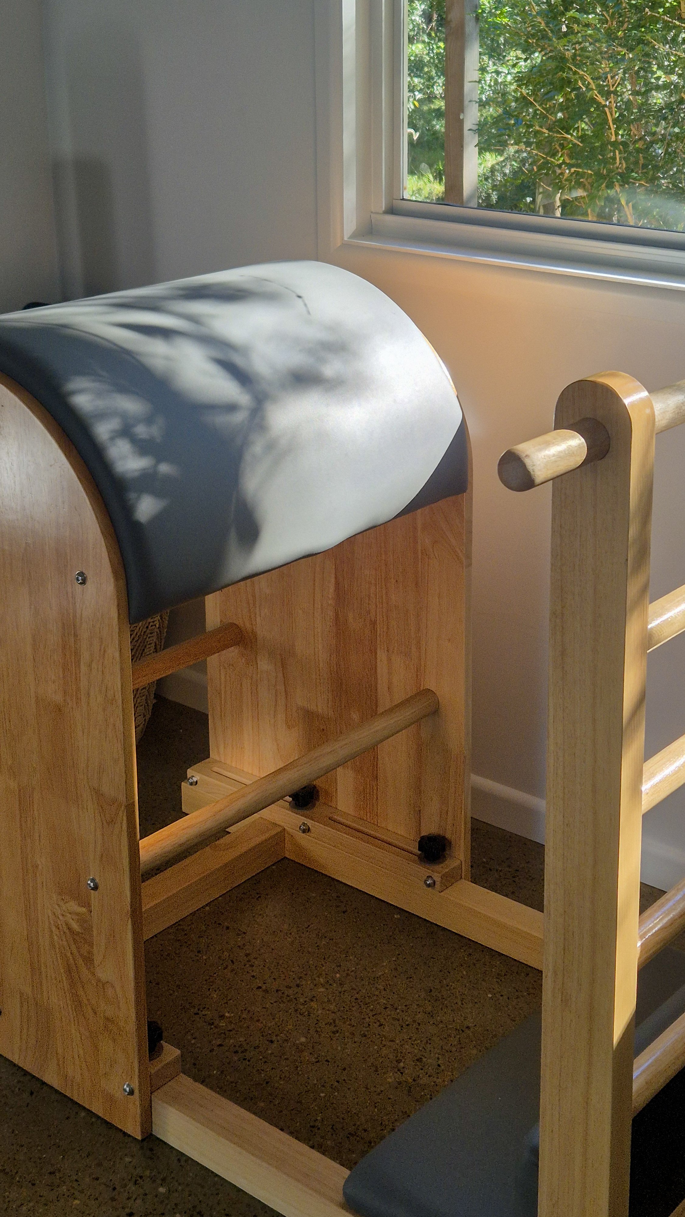 A wooden chiropractic adjusting or massage table with a dark gray padded surface, positioned near a window with greenery outside.