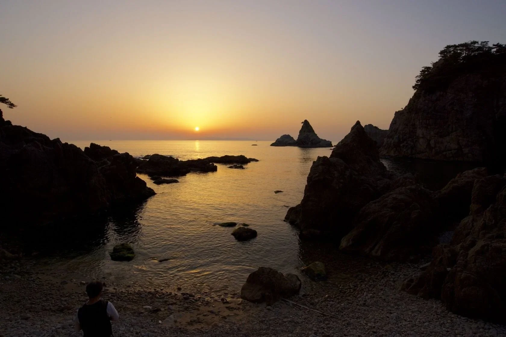 A rock cliff ocean landscape depicted at sunset.