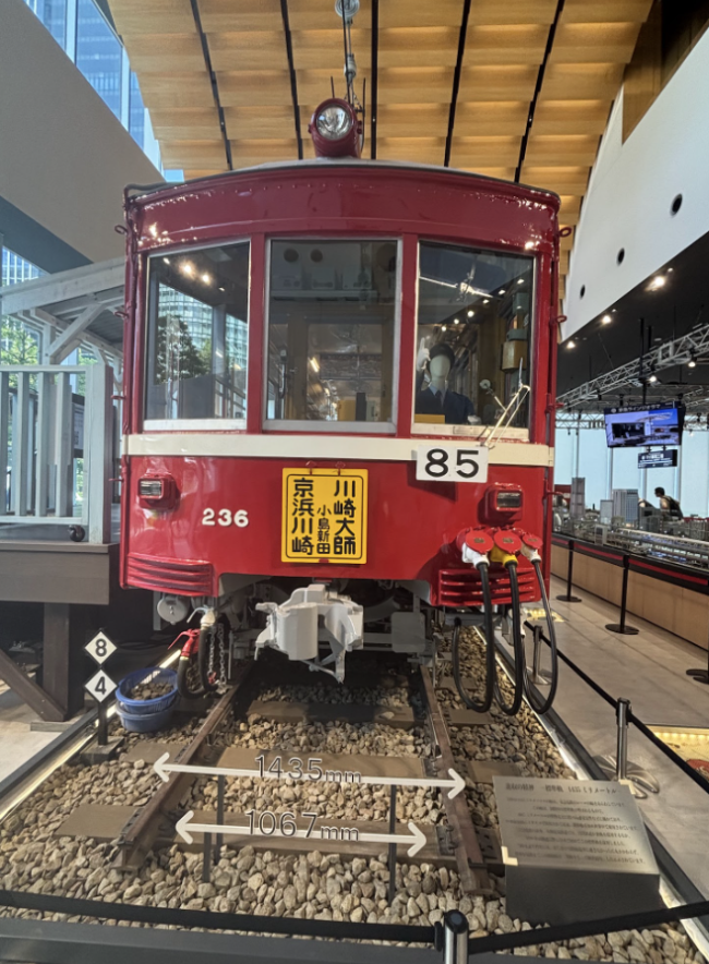 Life-size red train car is parked on a model platform.