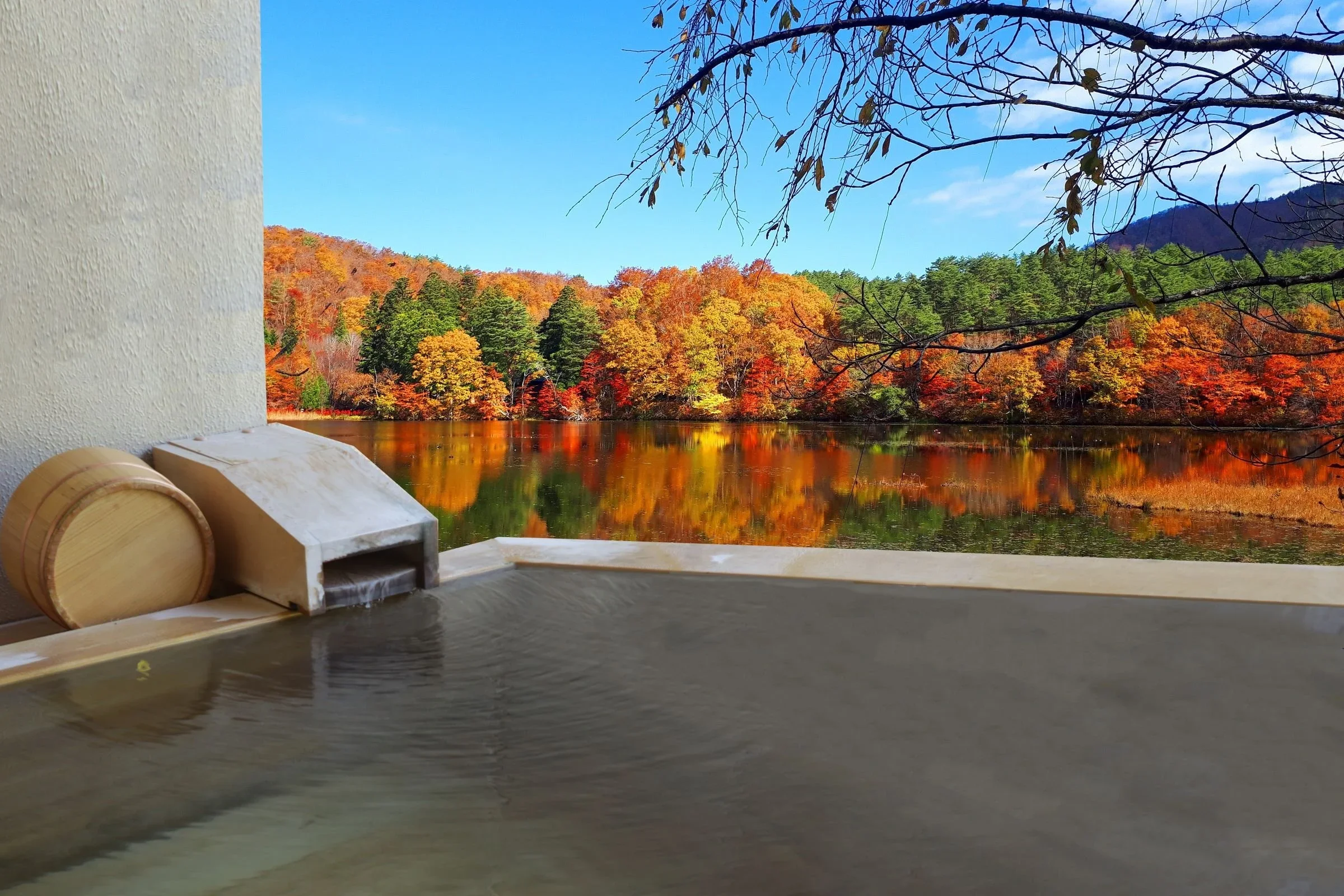 A private bath or onsen bath overlooks a Japanese lake and tree scene on a cloudless day in Japan.