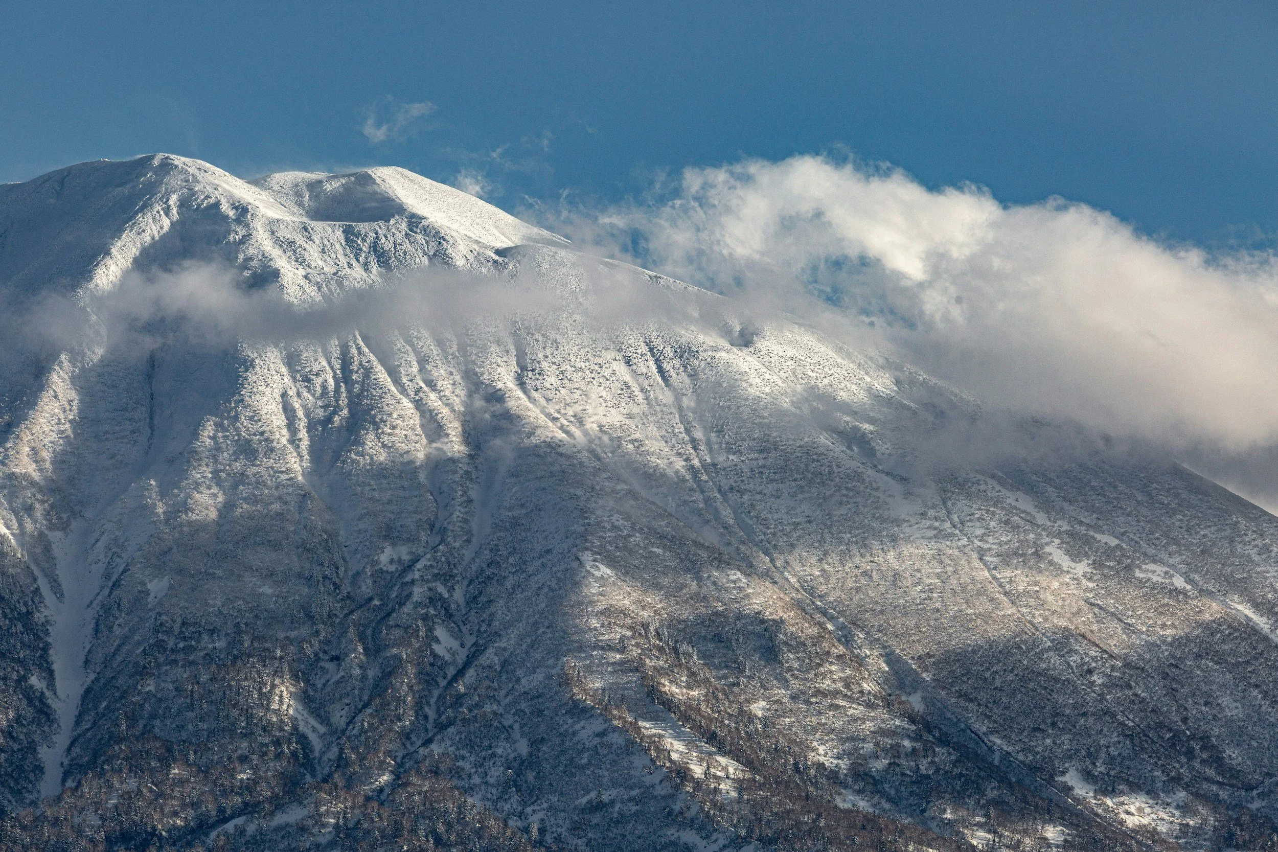 Image of the mountain that all 4 of the Niseko resorts are on covered 1/3 of the way down by cloud cover on a bluebird day.