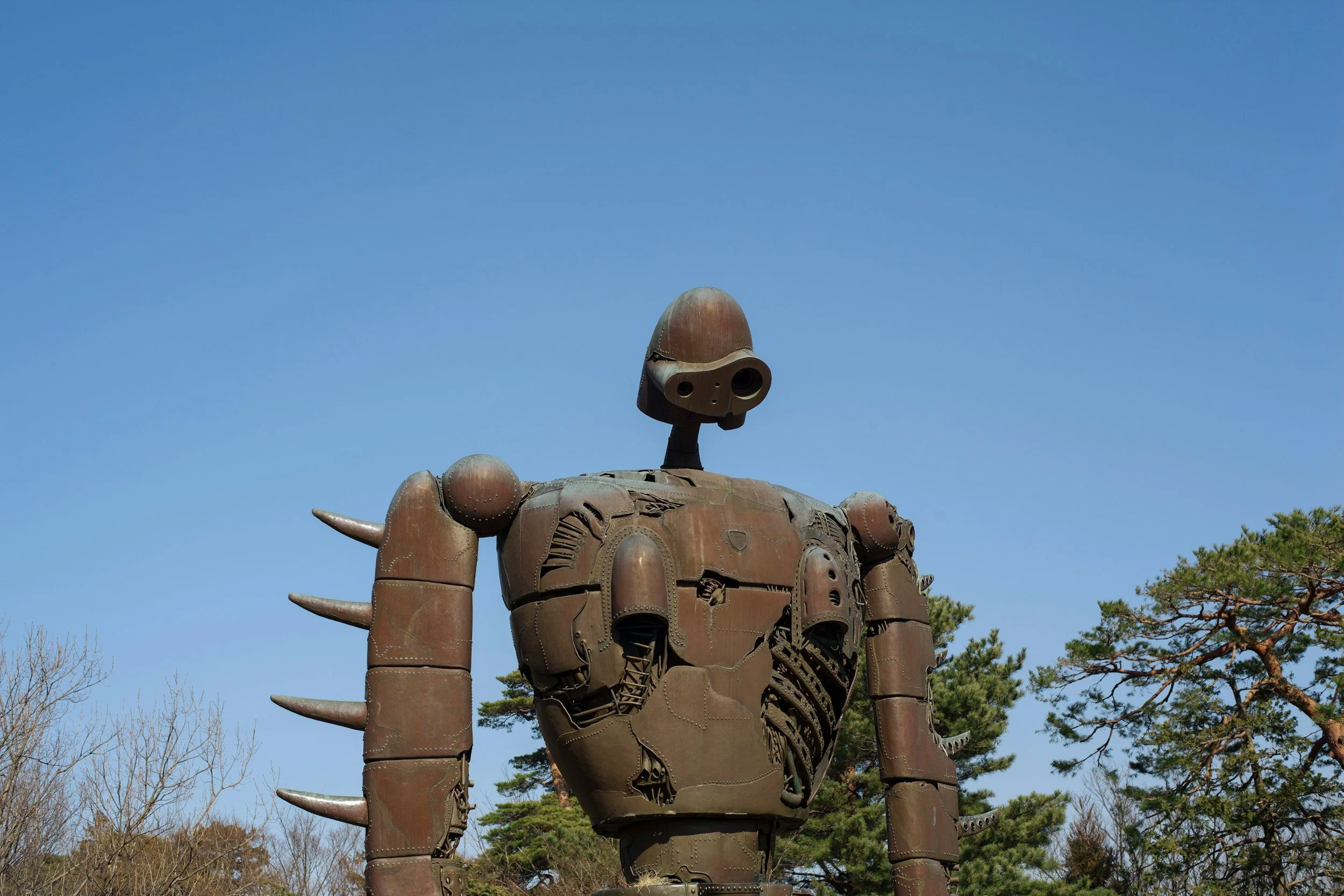 Image of a giant metal robot sculpture stands among the tree tops no a cloudless day at the Ghibli Museum in Mitaka, Japan.