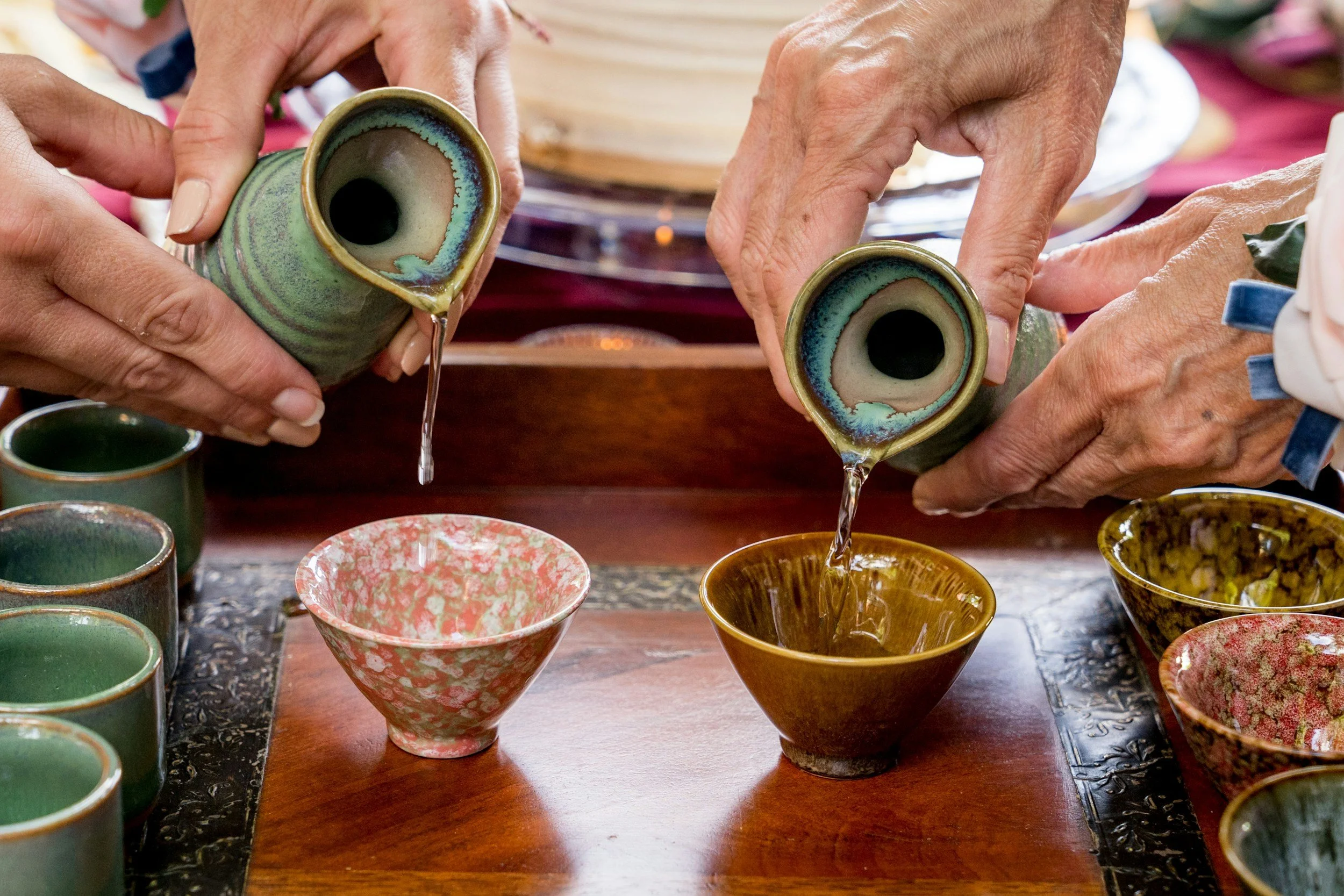 Two hands are pictured pouring sake into small sake cups.