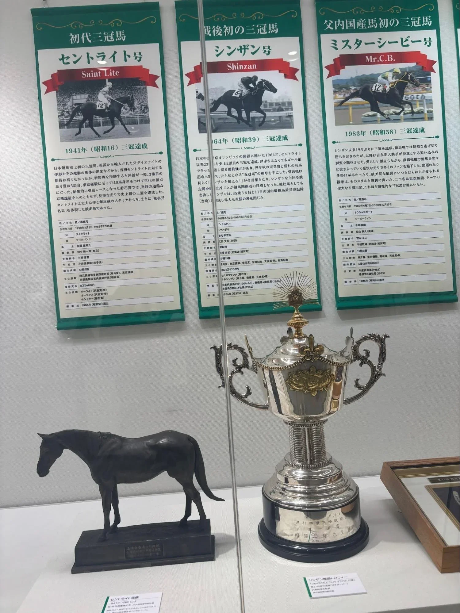 3 signs hang in a display case with a replica horse and a trophy on the bottom of the display. Signs describe the race horses Saint Lite from 1941, Shinzan from 1964, and Mr. C B from 1983.