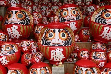 Different sized red Japanese ball dolls called Darumas with big black eyes and a mustache painted on them.