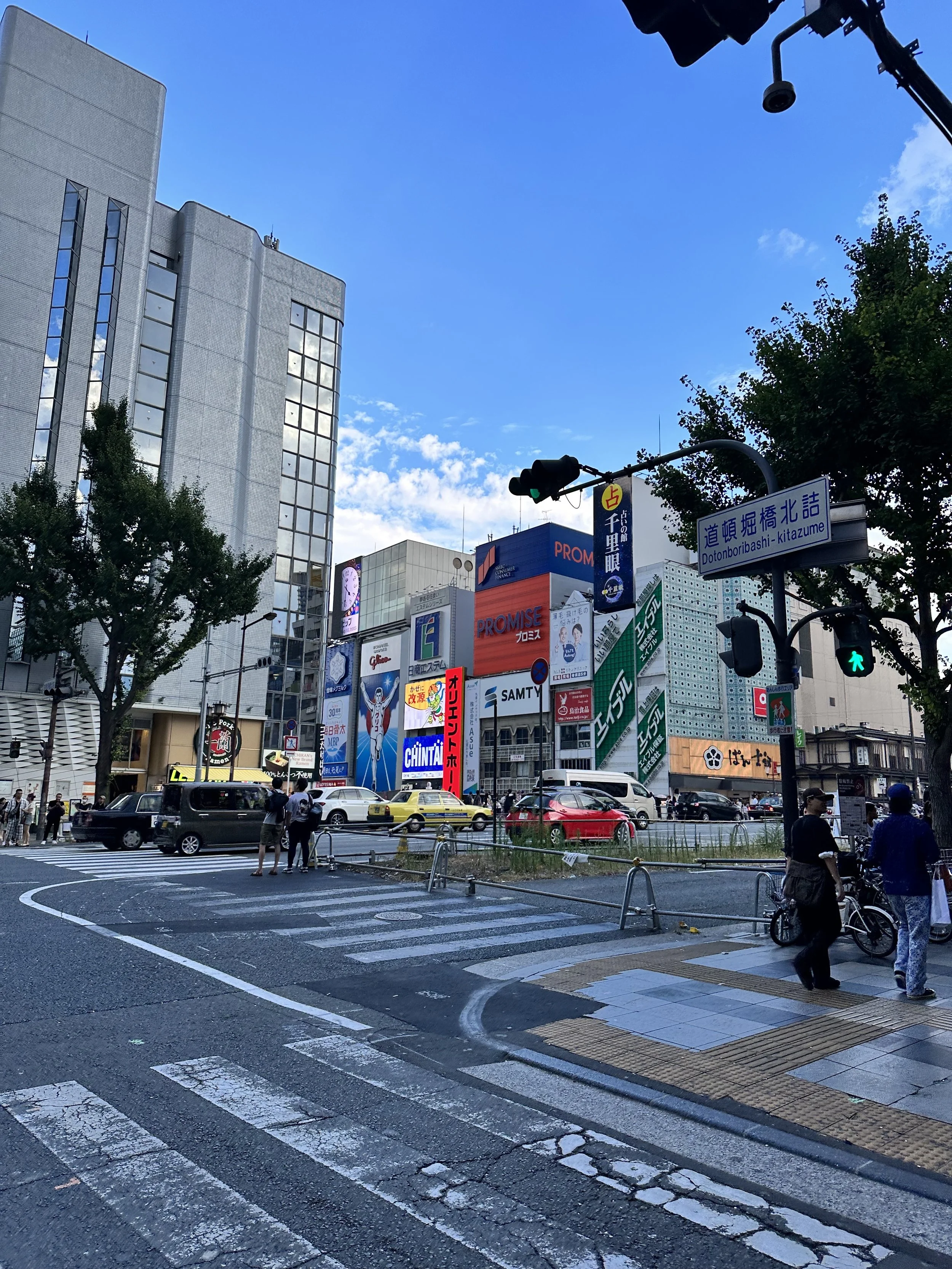 Intersection in Osaka Japan of buildings near a river and the Glico running man sign in the background. The intersection is in the foreground.