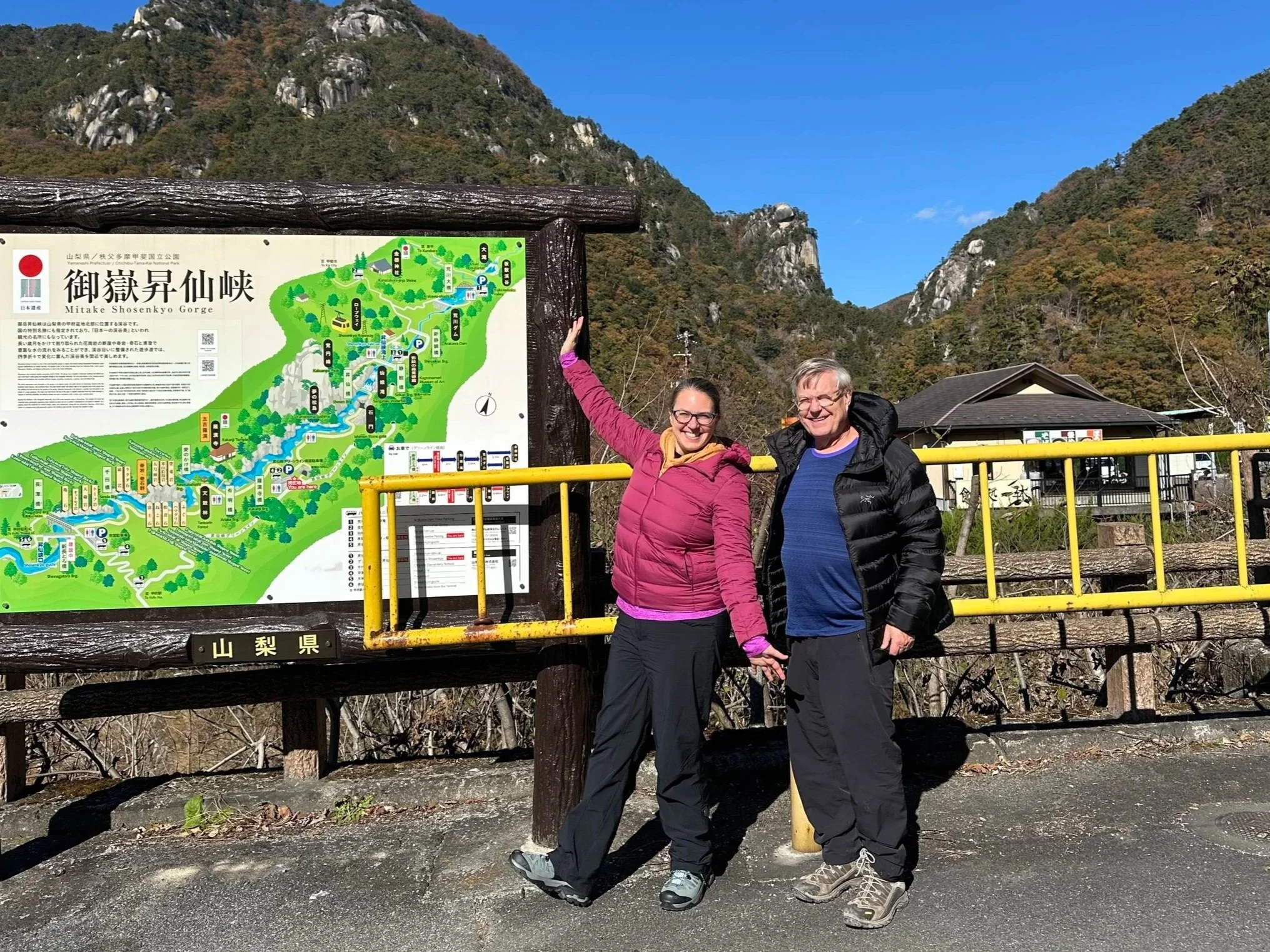 A father and a daughter explore a nature area in Japan, posing next to a map of the area.