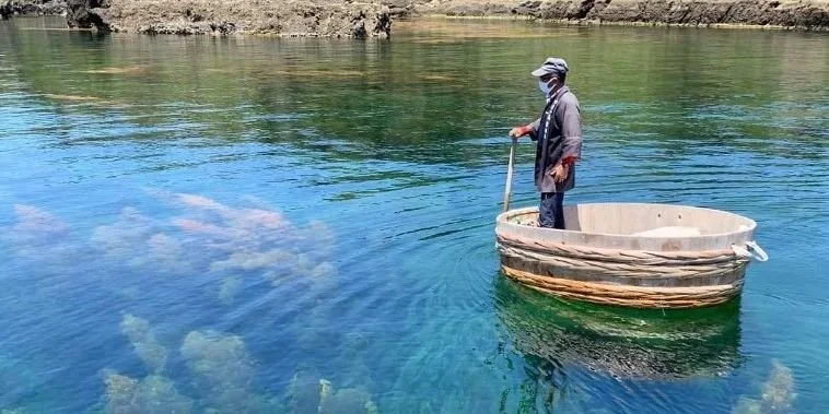 A man stands in a giant tub floating along the ocean.