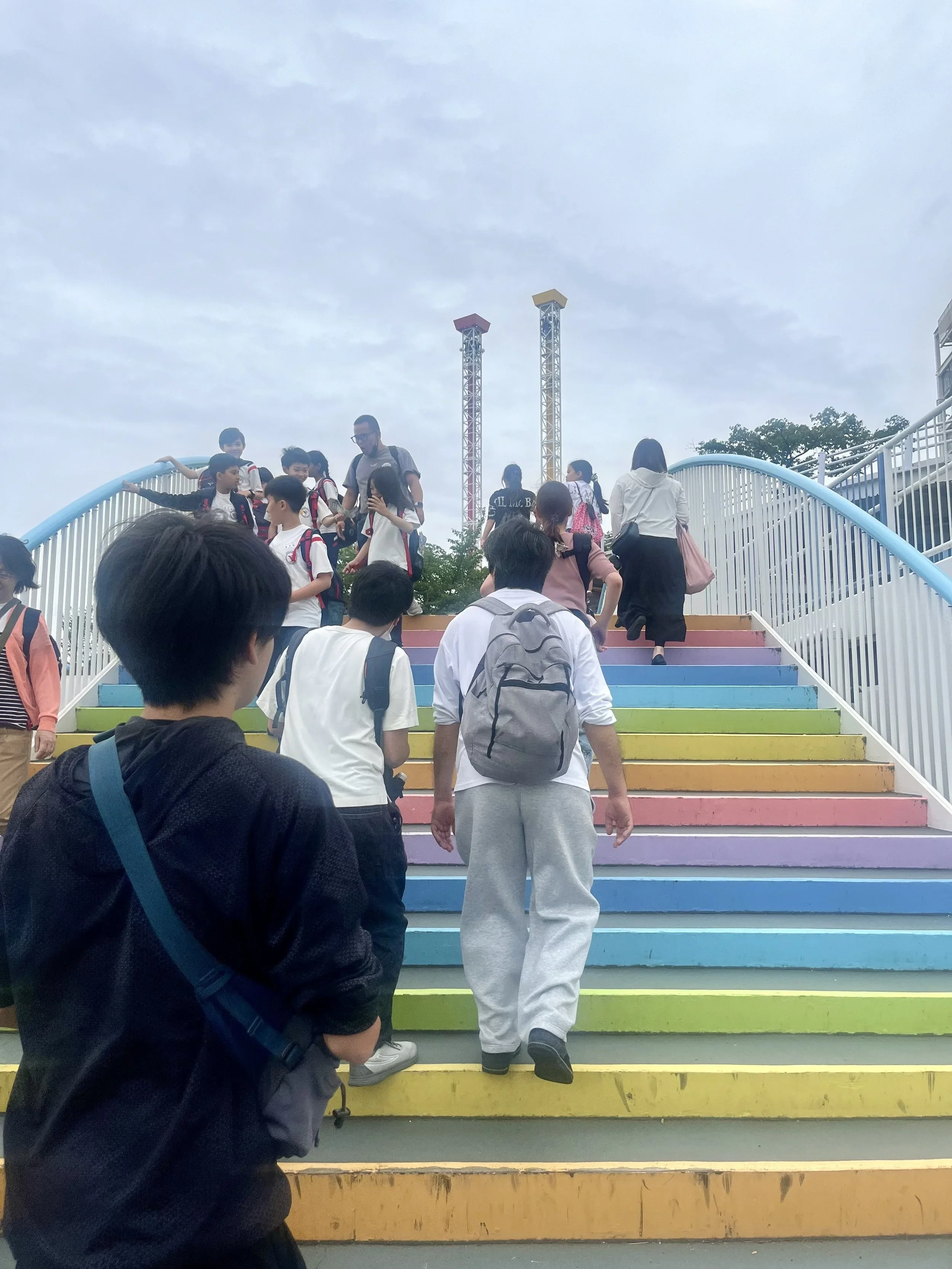 People walk over rainbow colored steps that comprise a foot bridge.