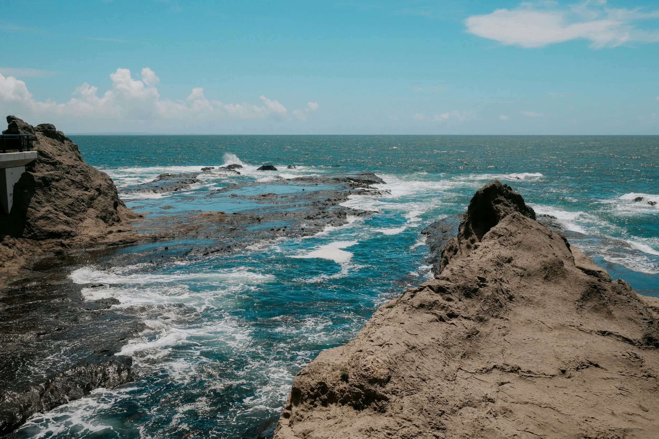 Image of the Japanese coastline near Tokyo, rocky cliffs with blue ocean waves and white peaks crashing against the cliffs.