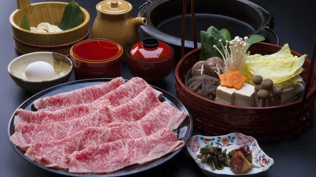 The raw ingredients for the traditional Japanese meal of Suki-Yaki is laid out on a black table.