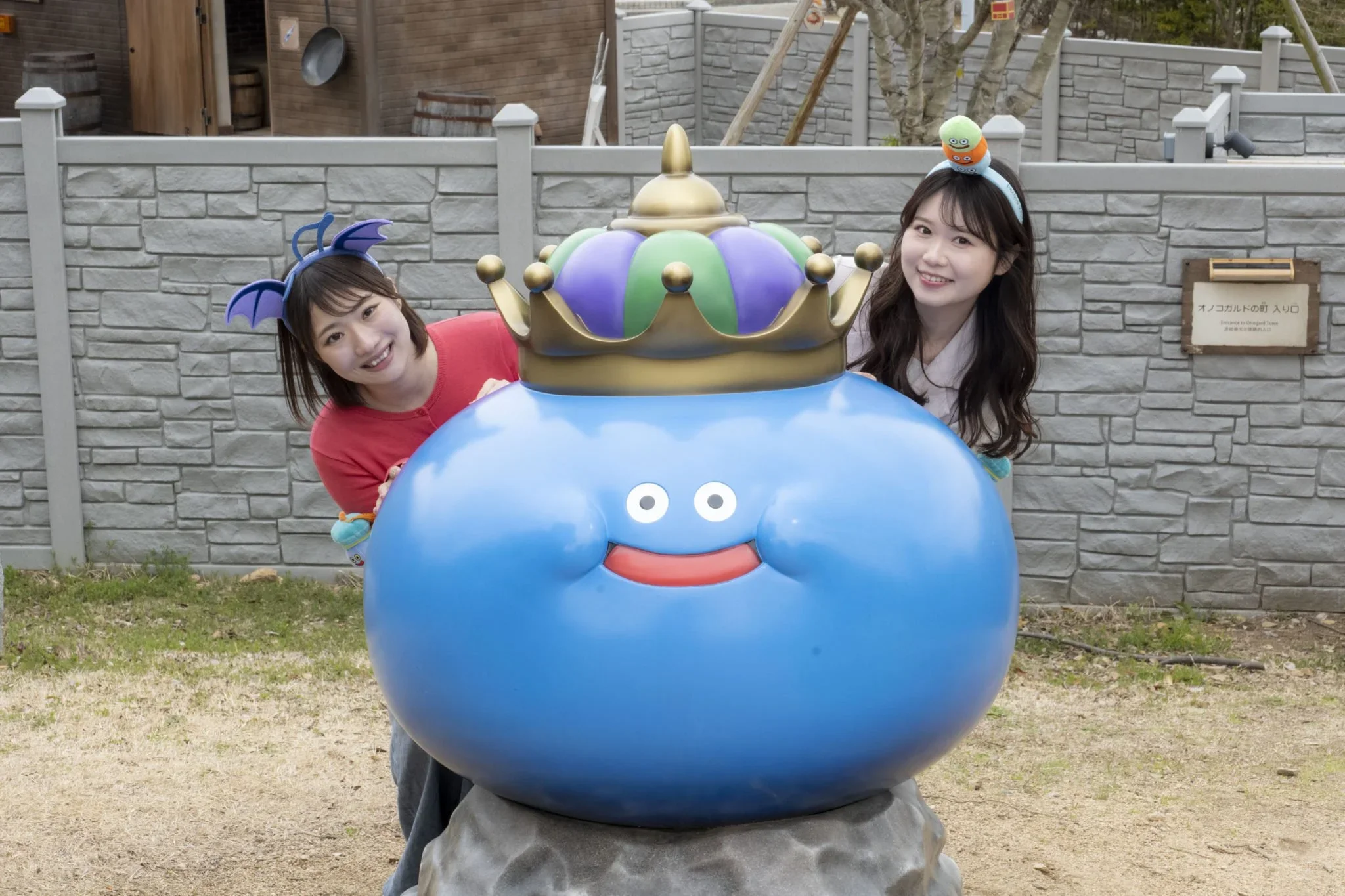 Dragonquest installation at Nijigen no Mori wth  a blue creature and a crown and two women pose peaking out behind it.
