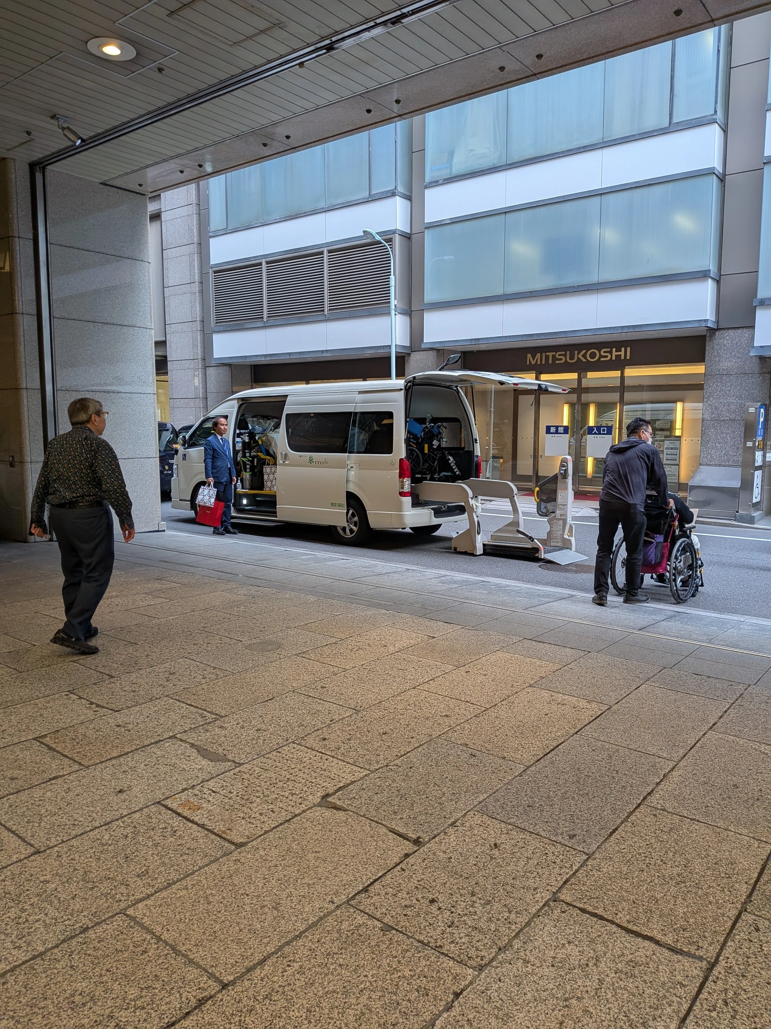 A private driver escorts a customer in a wheelchair to an accessible vehicle with a loading ramp.