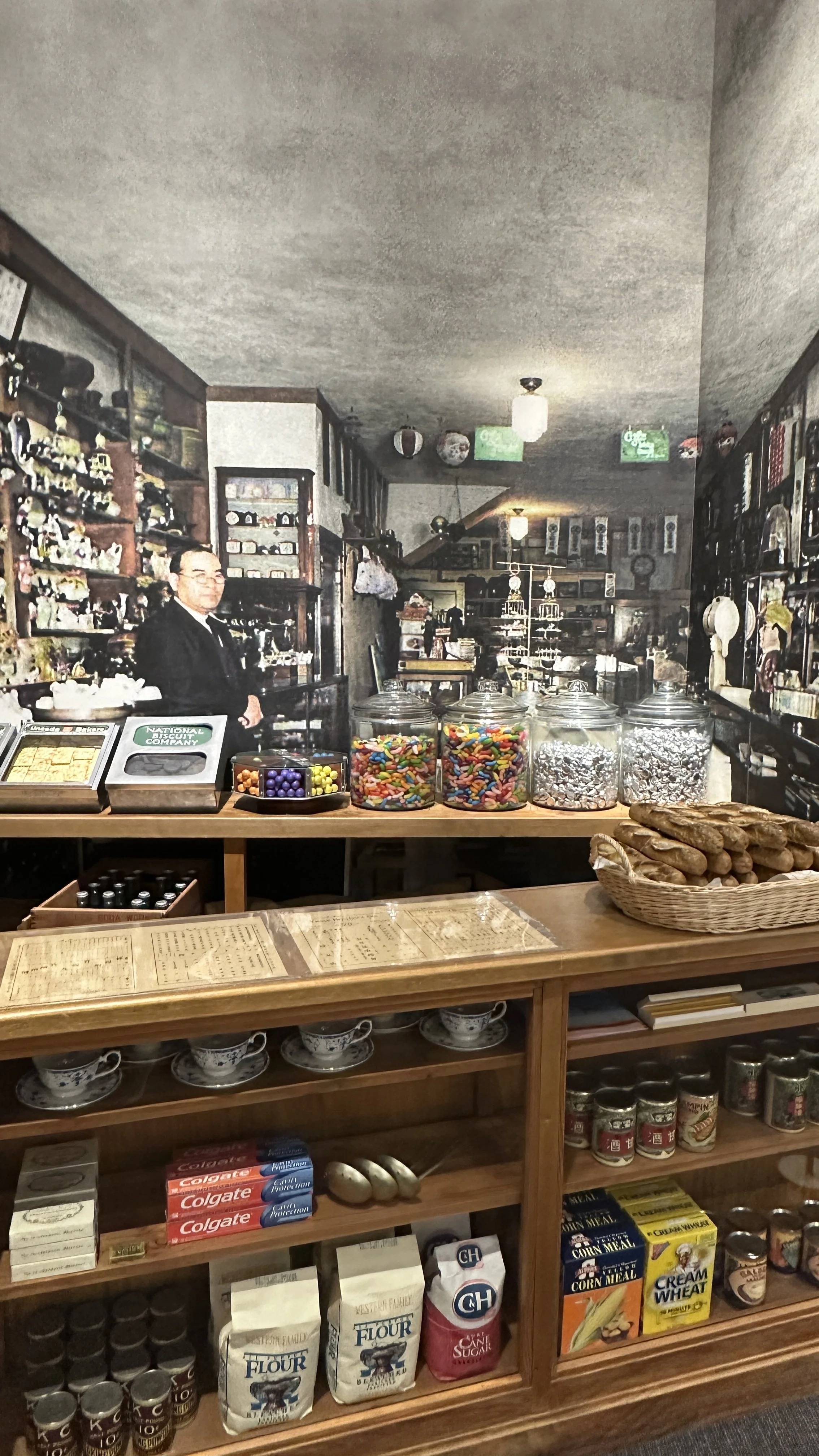 A photo of a Japanese man behind a display counter of retro Japanese and American food items.