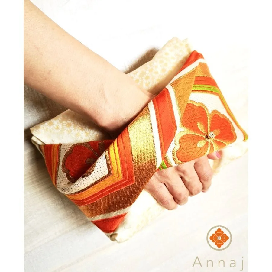 An orange and gold clutch bag made out of a vintage obi or kimono sash.