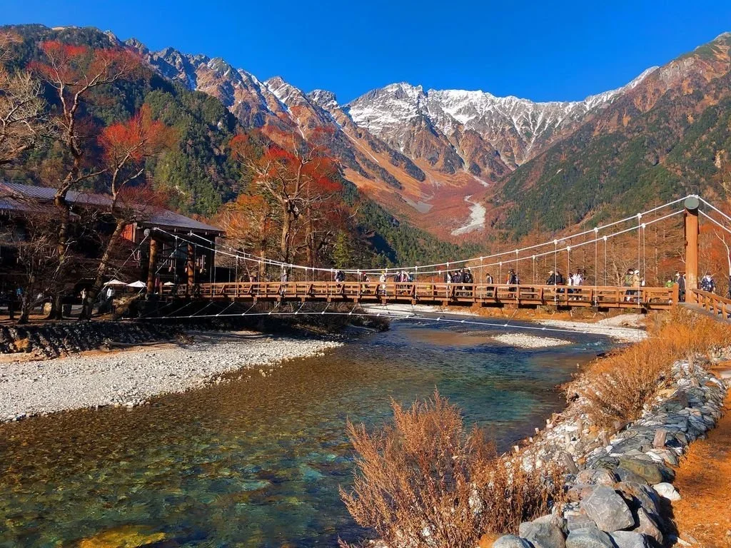 Fall scene in the Japanese alps of a metal bridge over a river with the mountain landscape in the background. Kamikochi, Japan.