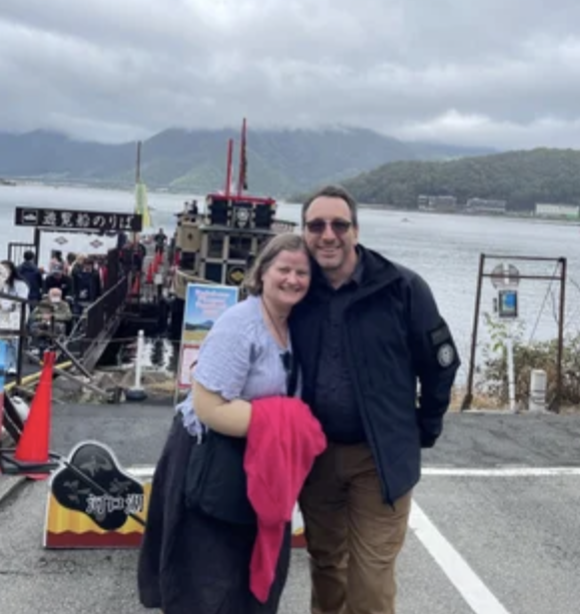 Two TokudaAw customers, a male and female, stand on boat dock in front of water on a cloudy day.