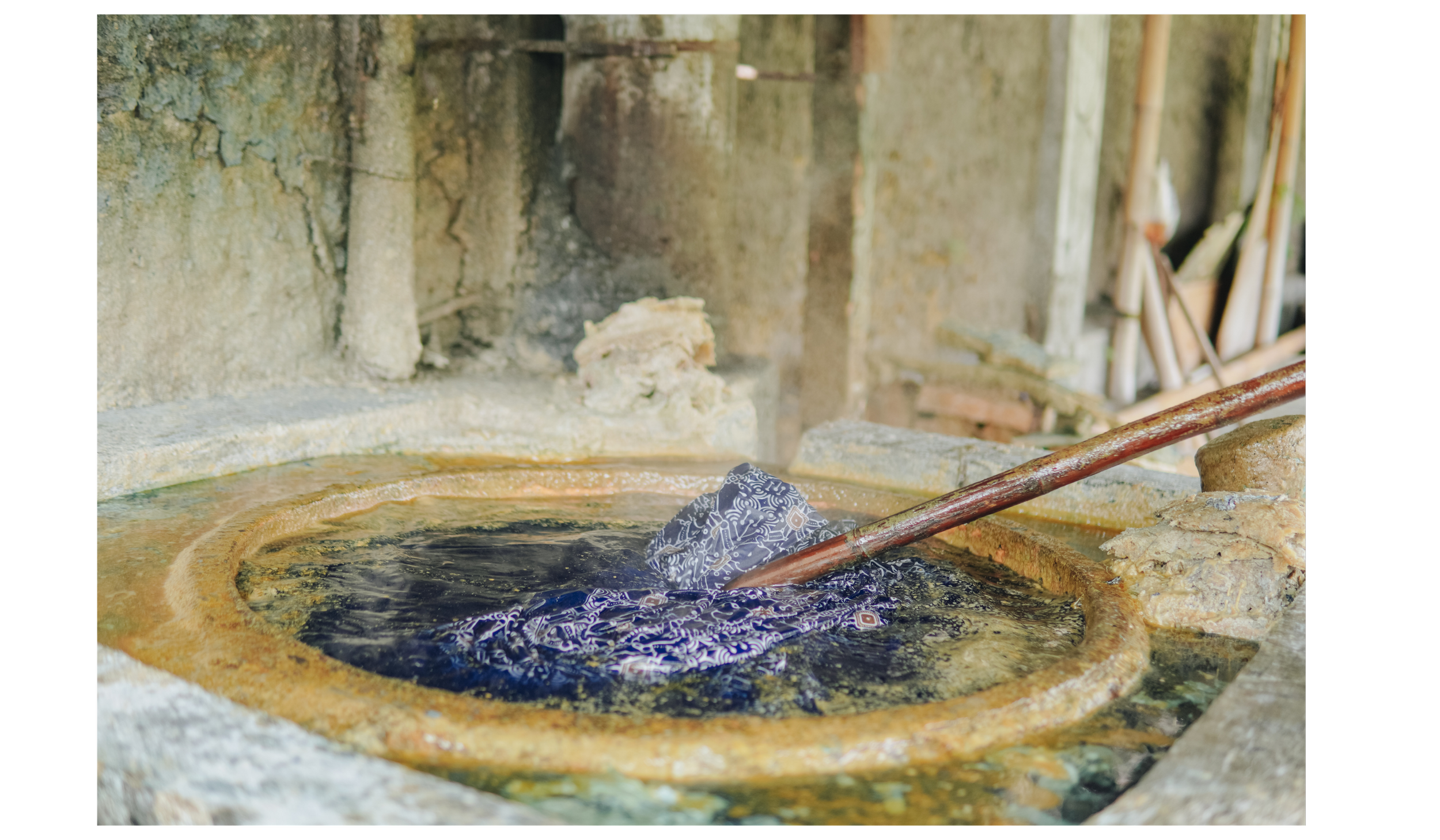 An image of an indigo vat with a rod stirring the indigo.