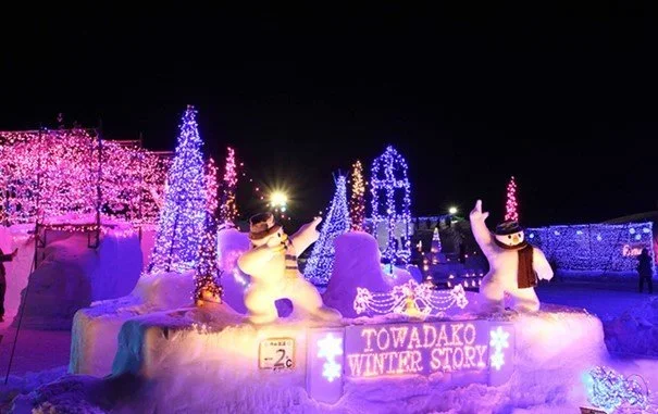 A nighttime illumination at lake Towada with snowmen and lit up Christmas trees.