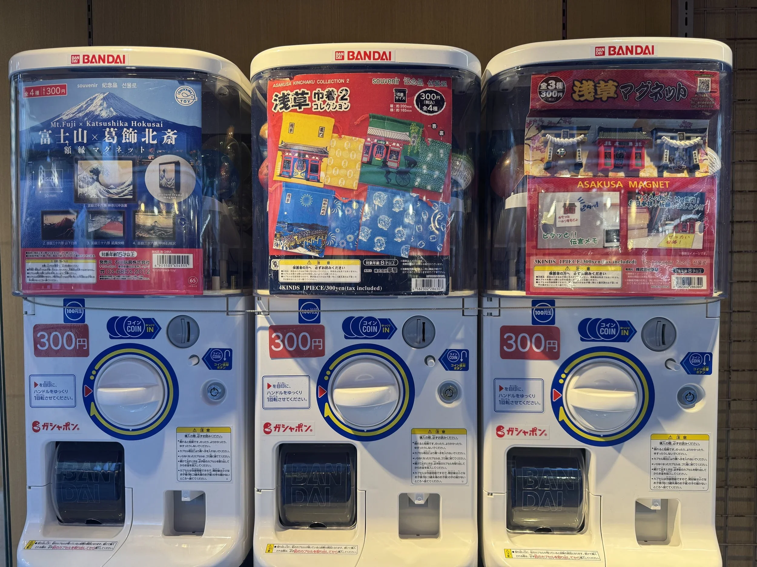 3 coin operated gatcha or random draw machines that deliver a random toy after spinning a dial.