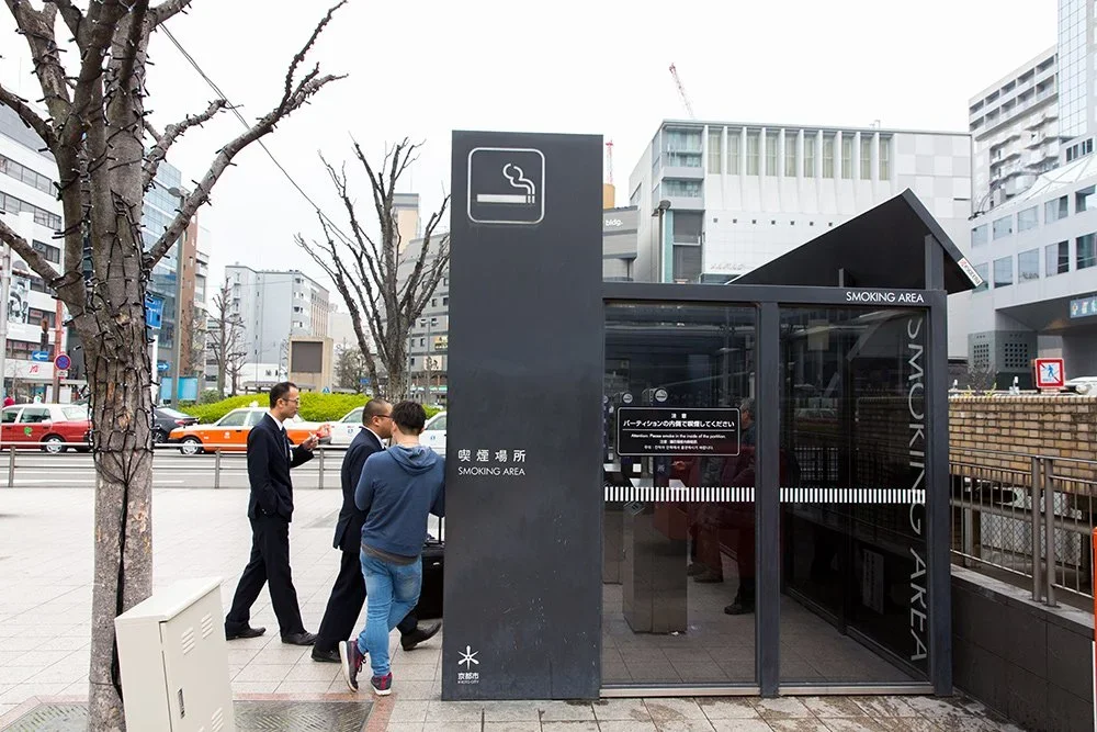 A smoking area enclosed structure on the corner of a Japanese street.