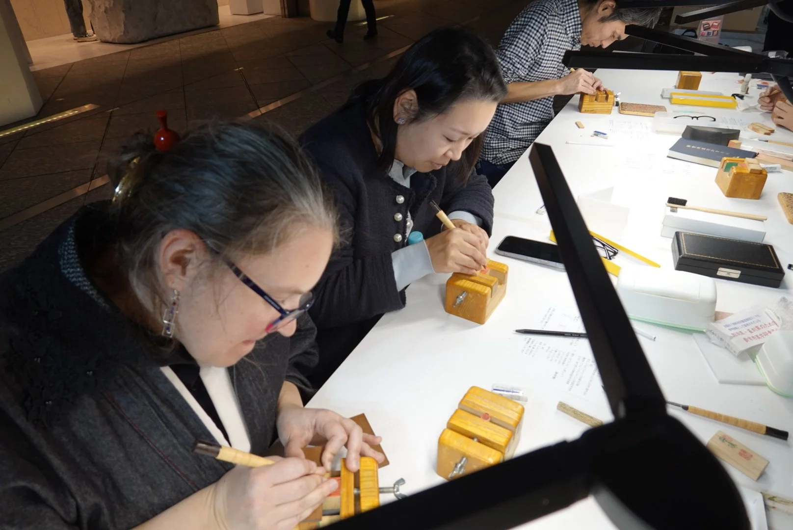 Women working at a table with traditional wooden Japanese stoneware and tools, possibly practicing calligraphy or a craft.