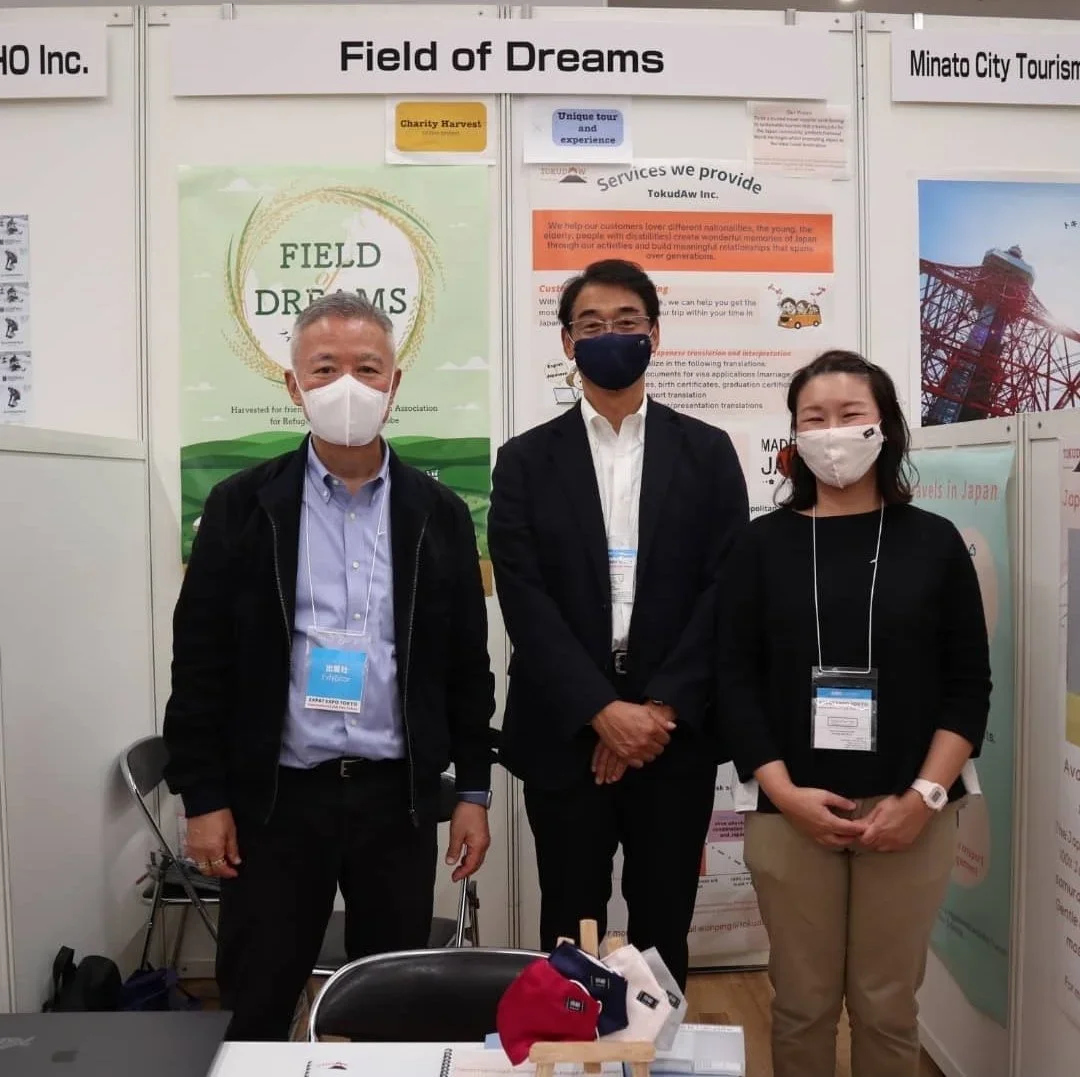TokudAw founders stand next to Charity Rice representative at a trade show poster session booth.