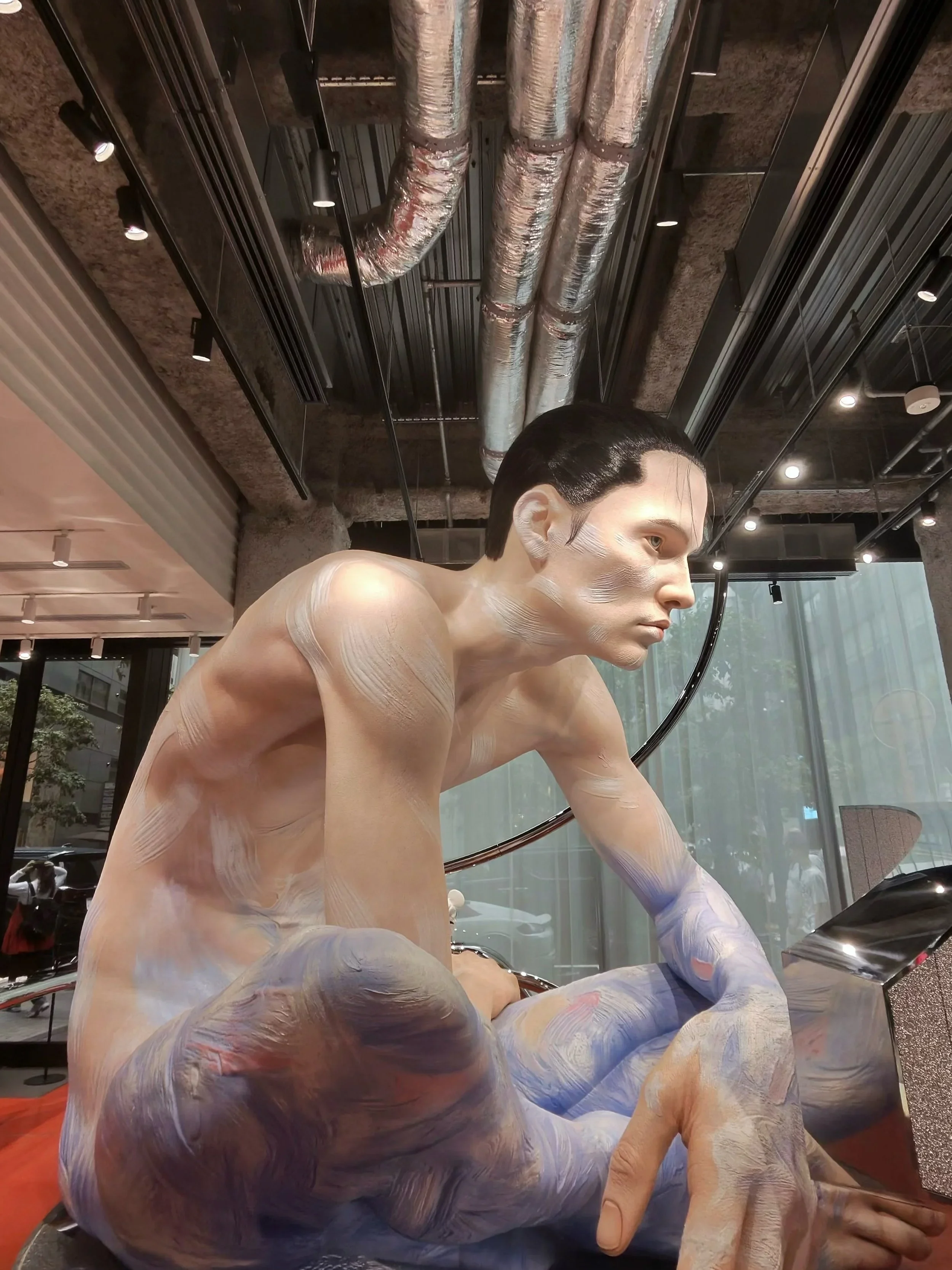 A sculpture of a man with a body painted in white and blue paint sitting cross legged and slumped over in the Ginza Gentle Monster store.