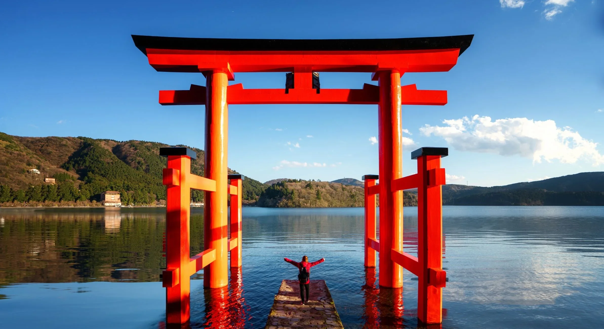 Red torii gate appears to float in water in a lake on a clear blue sky day, similar to the torii gate in Hiroshima.