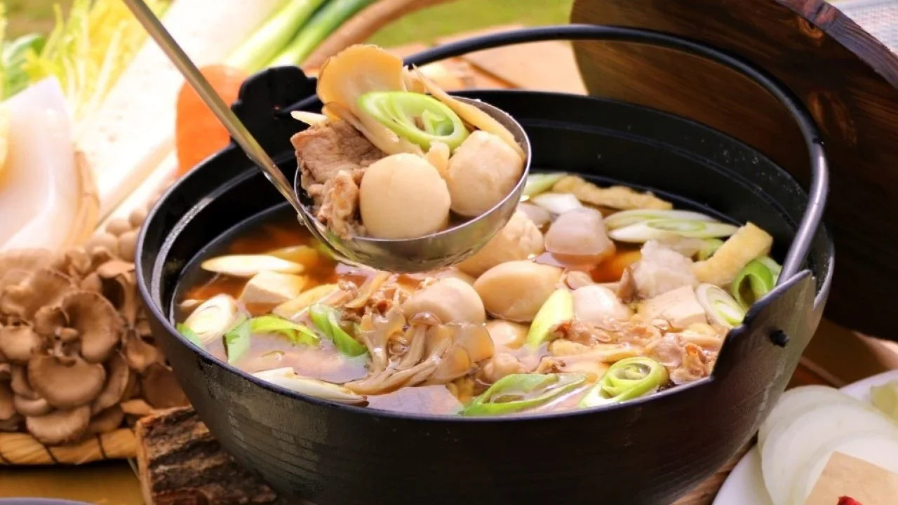 A Japanese hotpot stew soup with vegetables served from a ladle above a black pot with handle.