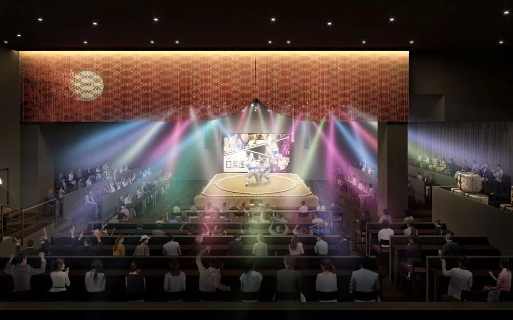 An audience views a sumo match in a 360 arena with stage lighting.